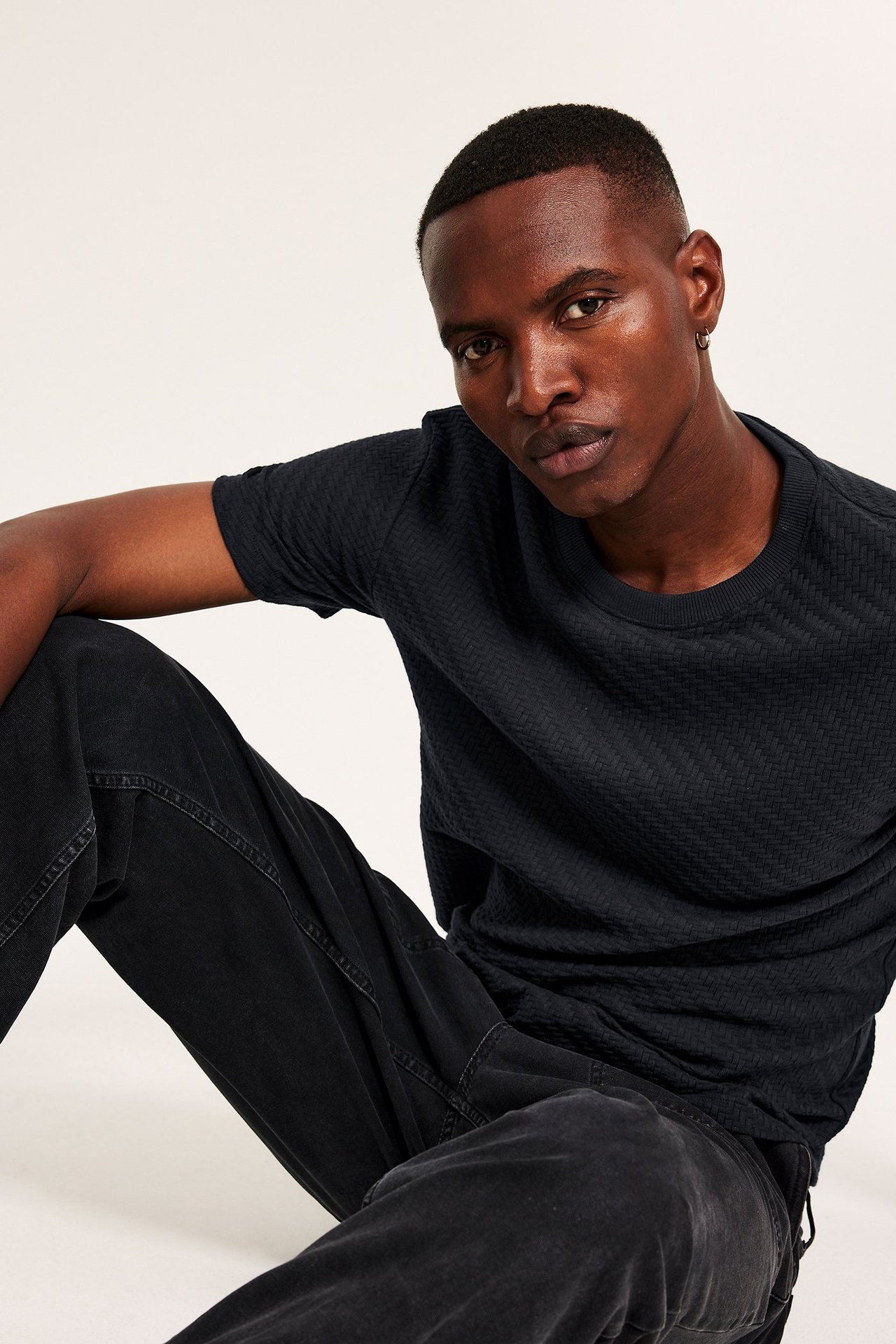 Zbliżenie z przodu mężczyzny w czarnym bawełnianym t-shircie ze wzorem strukturalnym i czarnych dżinsach.