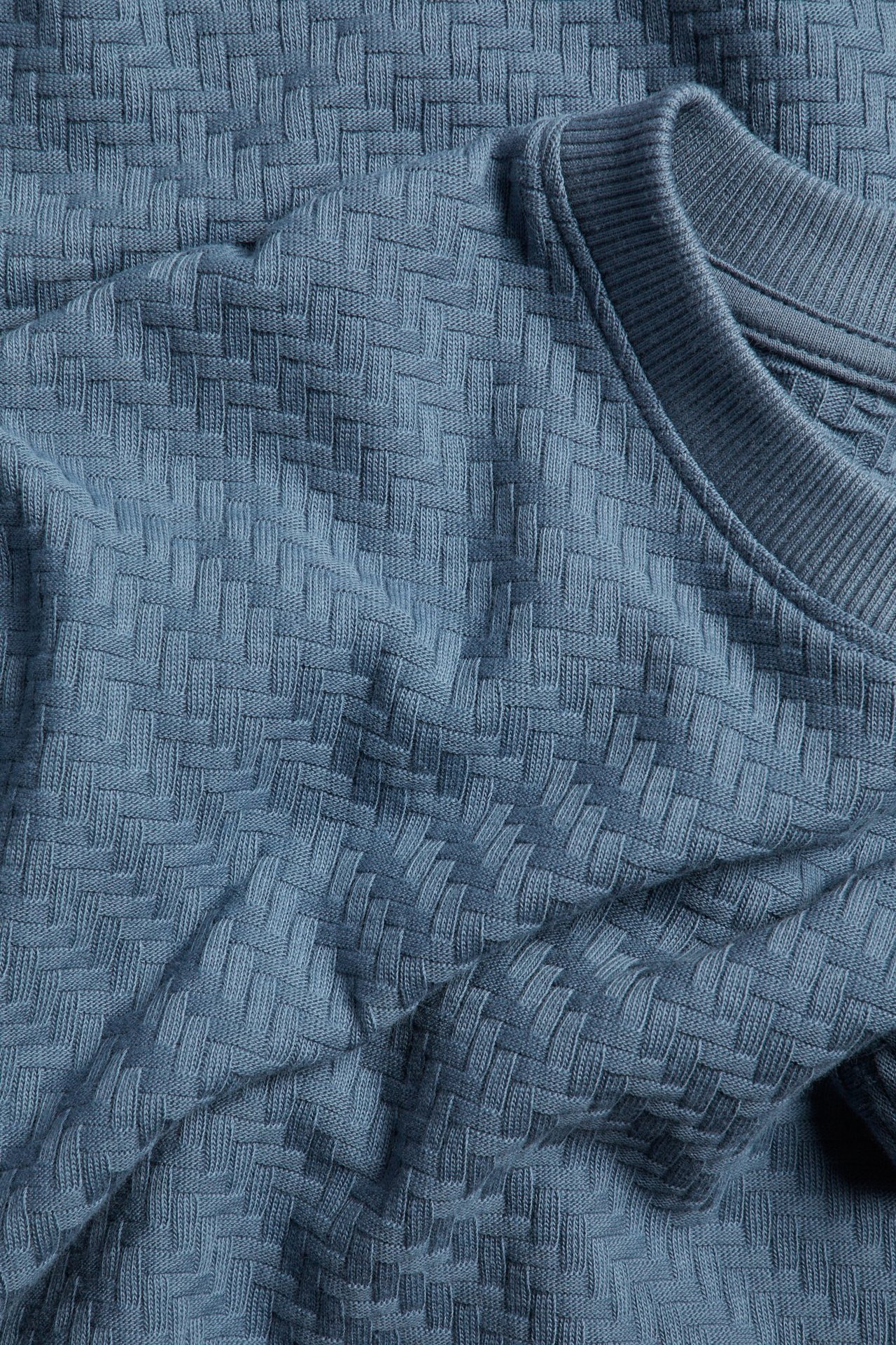 Zbliżenie na niebieski bawełniany T-shirt ze strukturalnym wzorem i prążkowanym dekoltem.