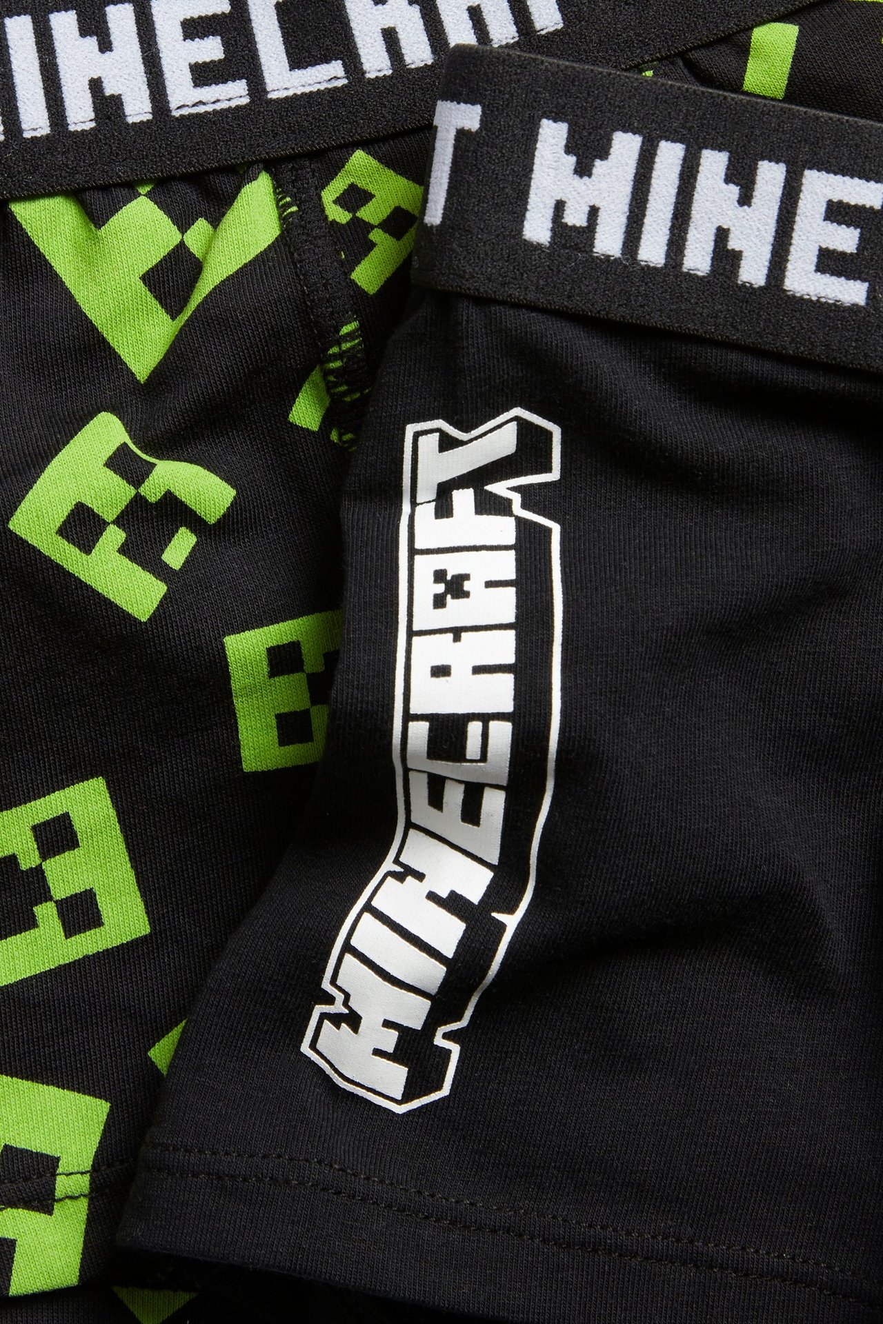 Zbliżenie dwóch czarnych bokserek Minecraft dla dzieci: jedne zielono-wzorzyste, drugie z białym napisem.