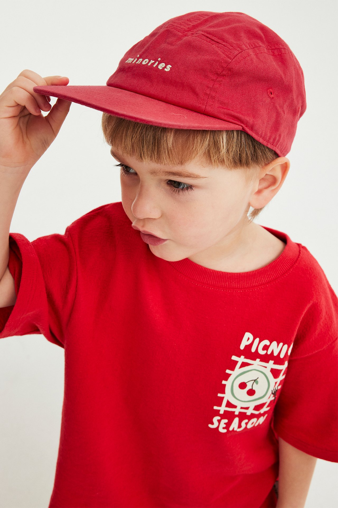 Nærbilde av et barn iført en rød bomullscaps med 'minorities'-broderi og en rød t-skjorte.