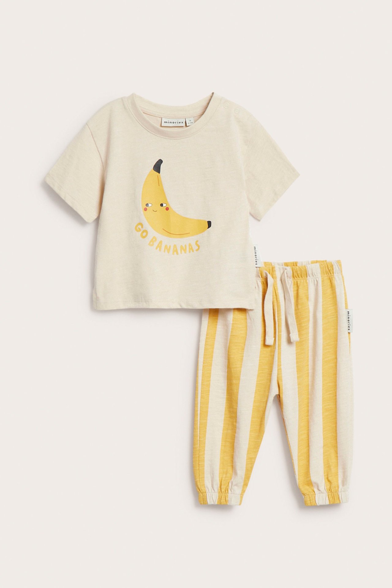 Widok z przodu: niemowlęcy kremowy bawełniany T-shirt z żółtym nadrukiem banana i pasujące żółte spodnie w paski.