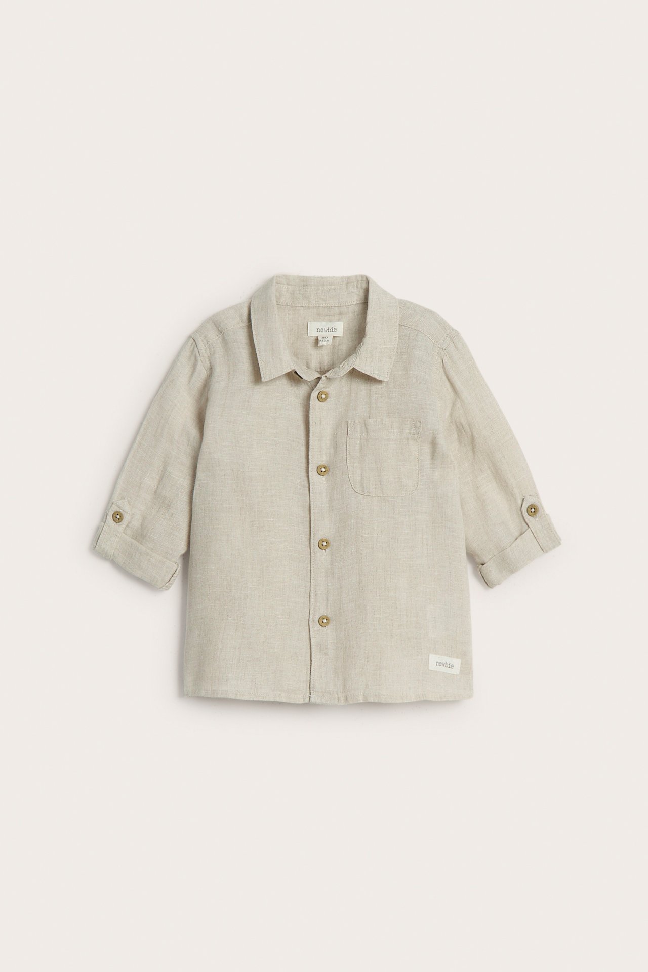 Frontvisning av en lys beige linskjorte for barn med krage, knapper, opprullede ermer og brystlomme.