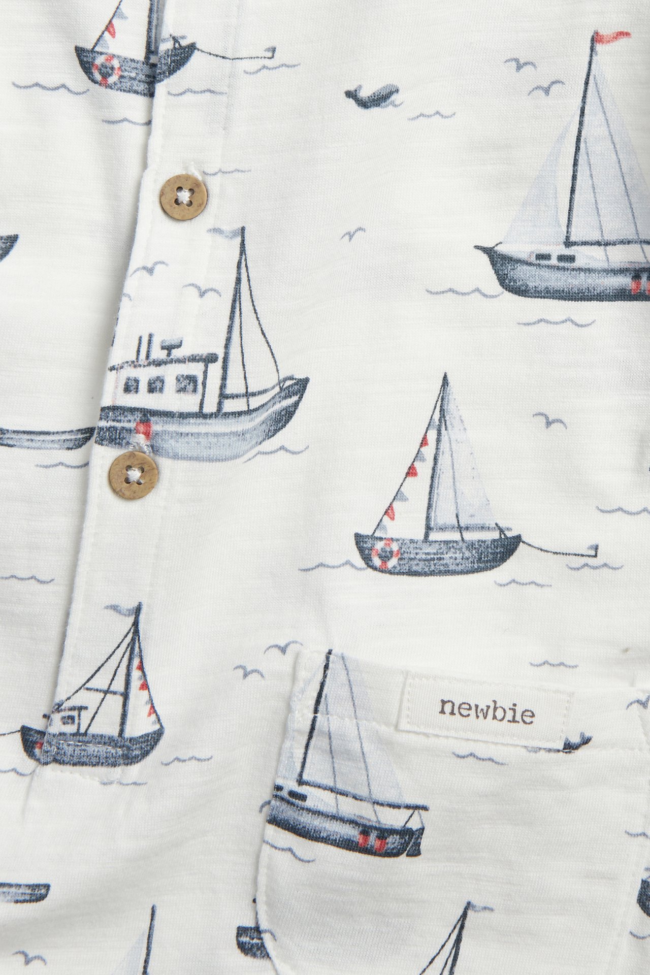 Närbild av en offwhite romper i slubtrikå med segelbåtsmönster och träknappar.