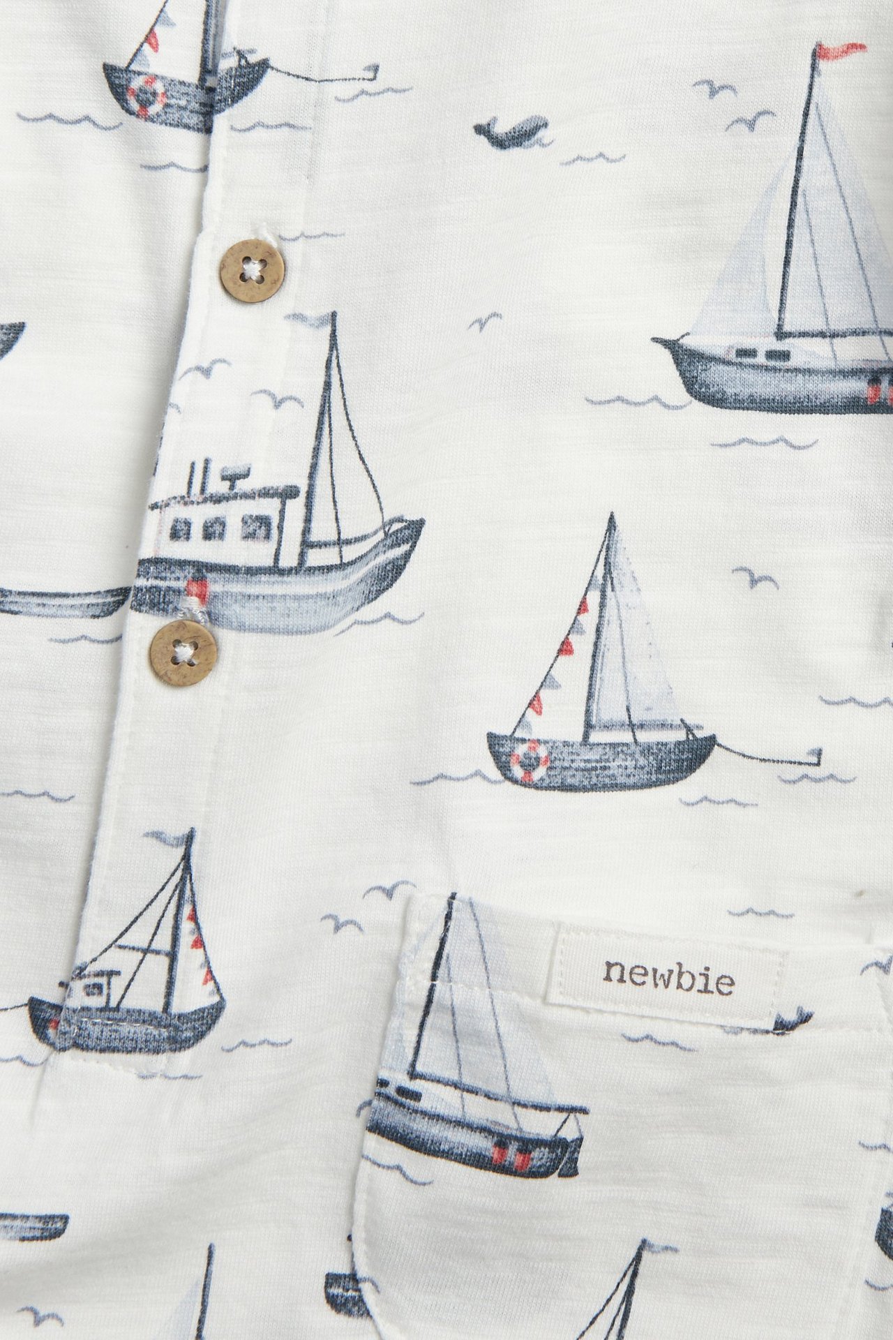 Zbliżenie: biały romper z bawełny slub w żaglówki, z drewnianymi guzikami.