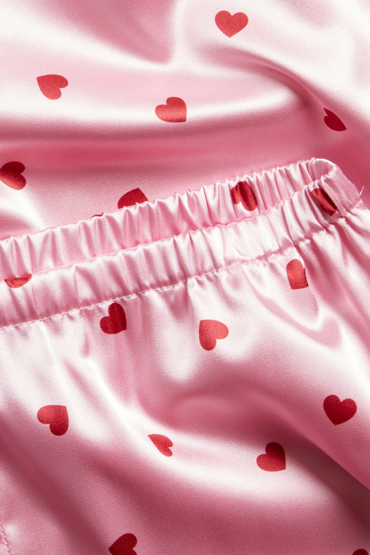 Nærbilde av lys rosa satengpyjamas med rødt hjertemønster og elastisk midje.