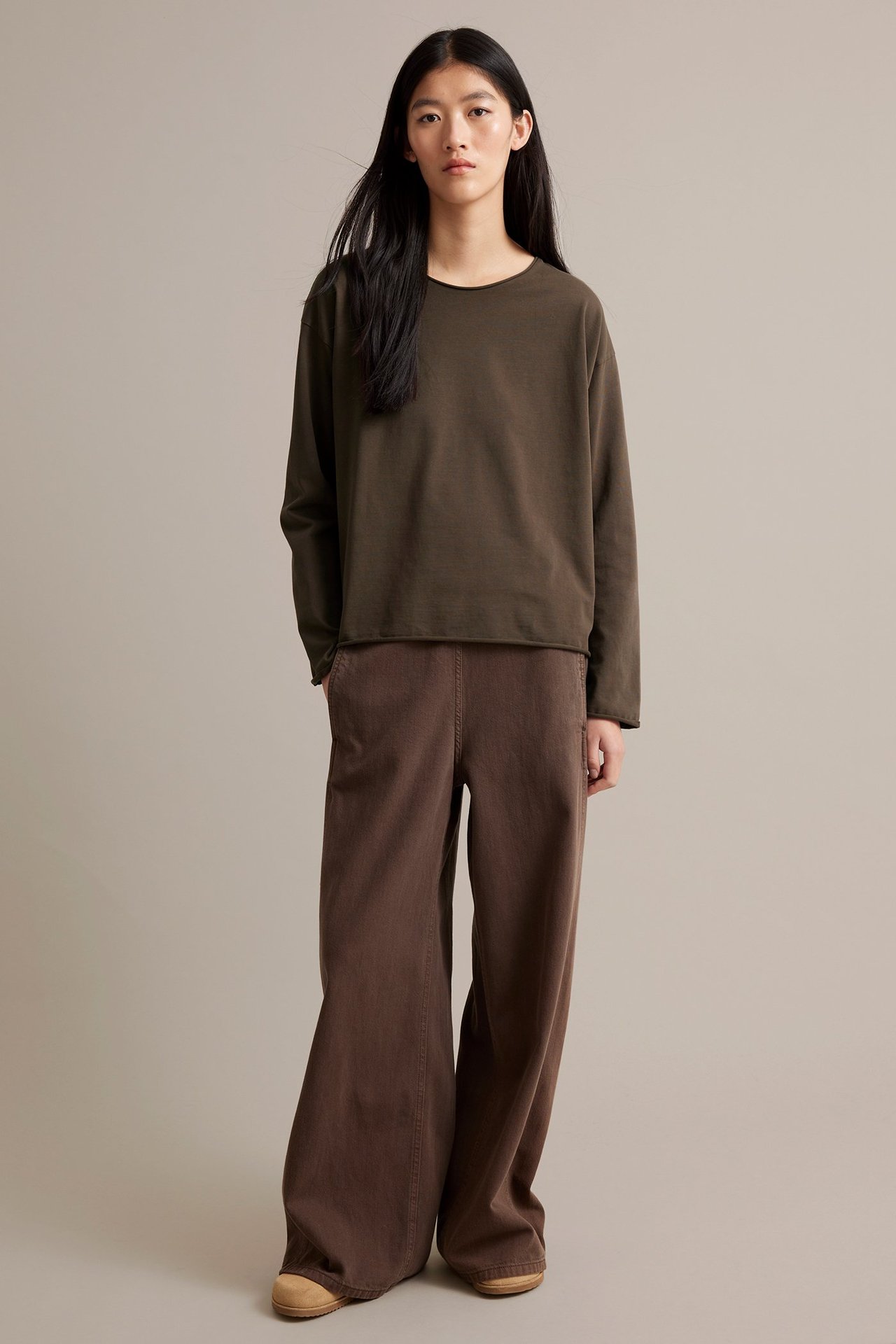 Nainen pukeutunut tummanruskeaan pitkähihmaiseen puseroon paksusta jerseystä, reunoissa rispaantunut.