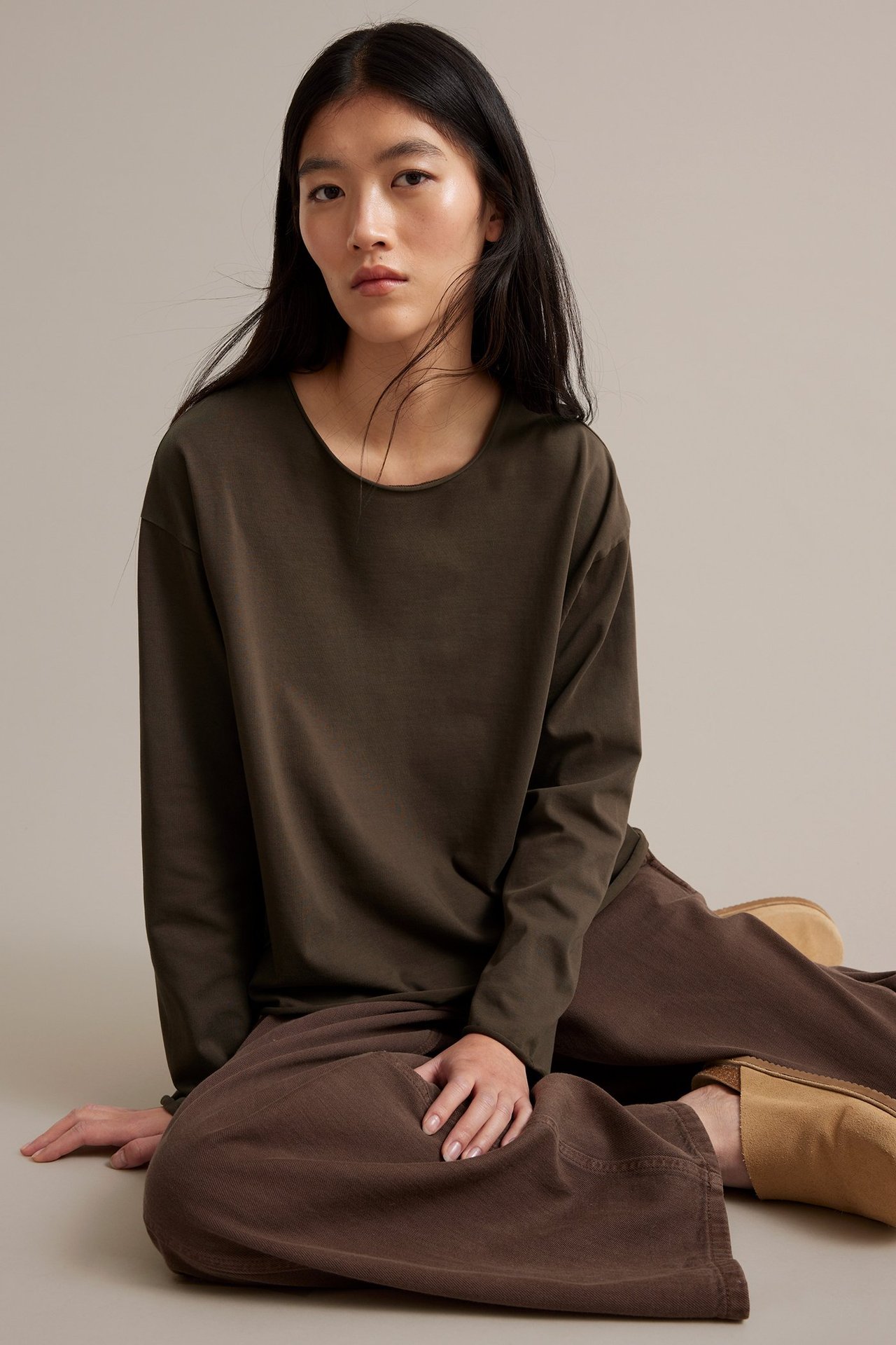 Nainen tummanruskea pitkähihaisessa topissa paksua trikoota, raajat kiepsahtaneet, lattialla istuva.