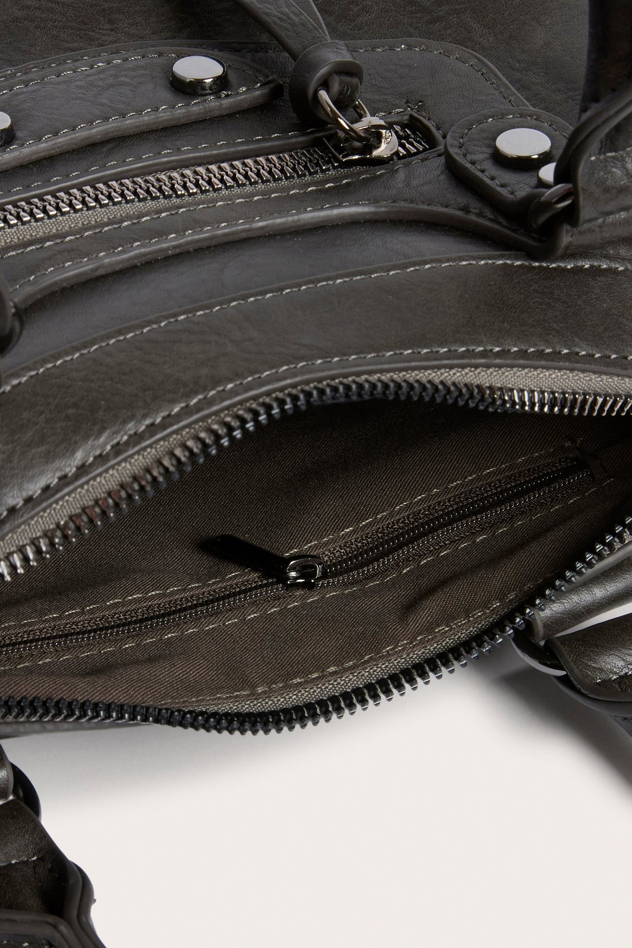 Nærbilde av en grå veske i imitert skinn med flere glidelåslommer og sølvfargede trykknapper.