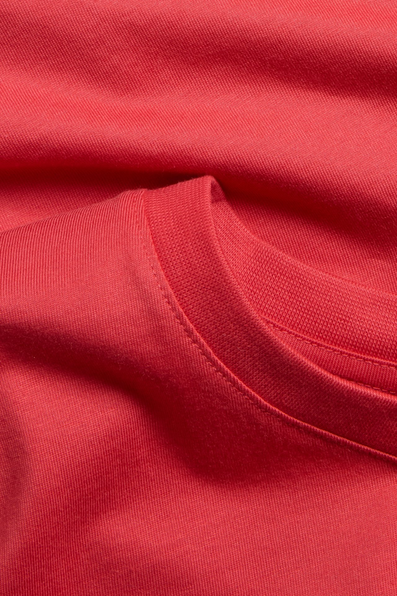 Nærbilde av en ensfarget rød bomulls-T-skjorte, som viser stoffteksturen og den ribbestrikkede runde halsen.