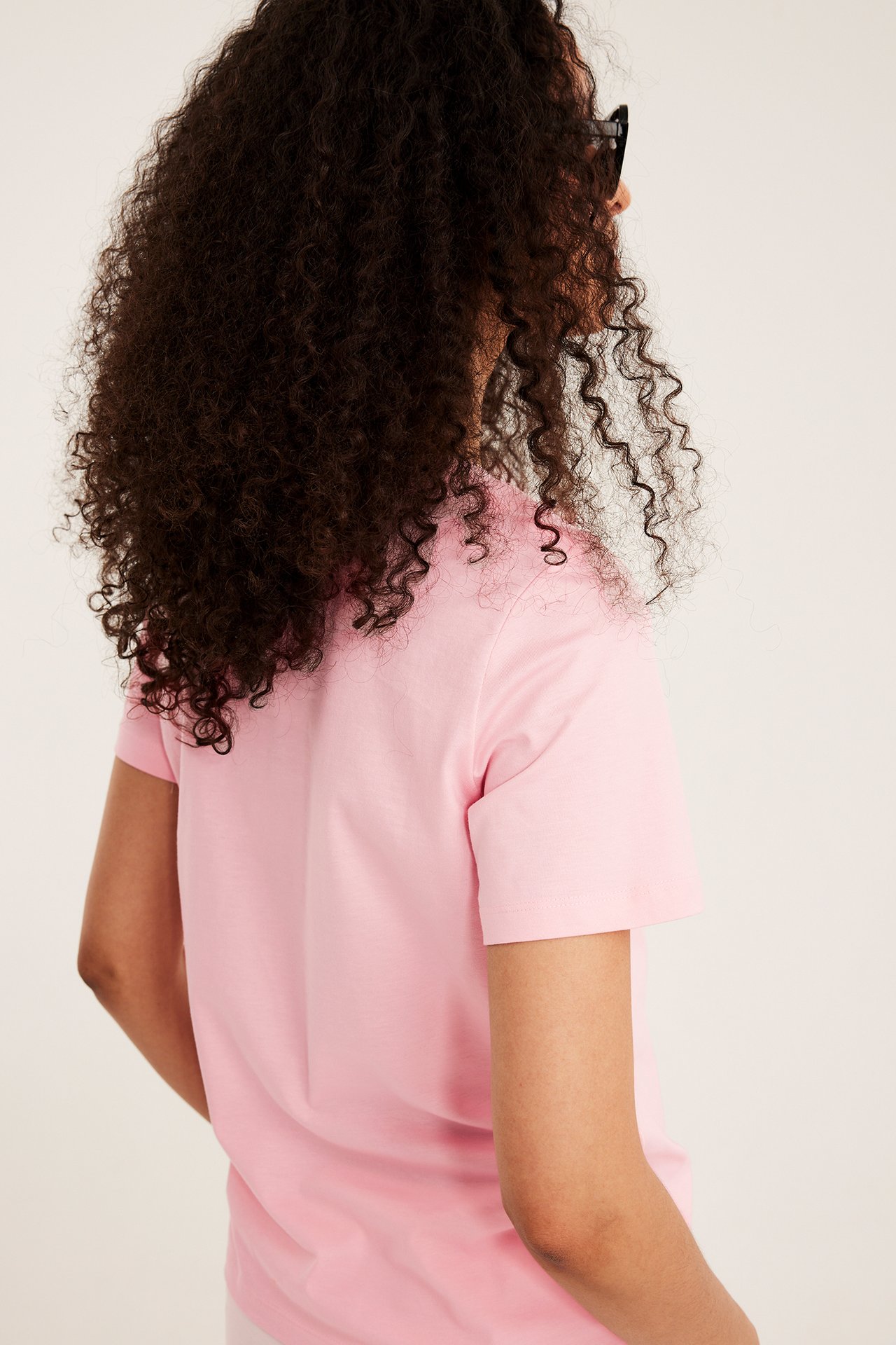 Naisen taka- ja sivukuva yllään pinkki, suoraleikattu puuvilla T-paita mustilla aurinkolaseilla.