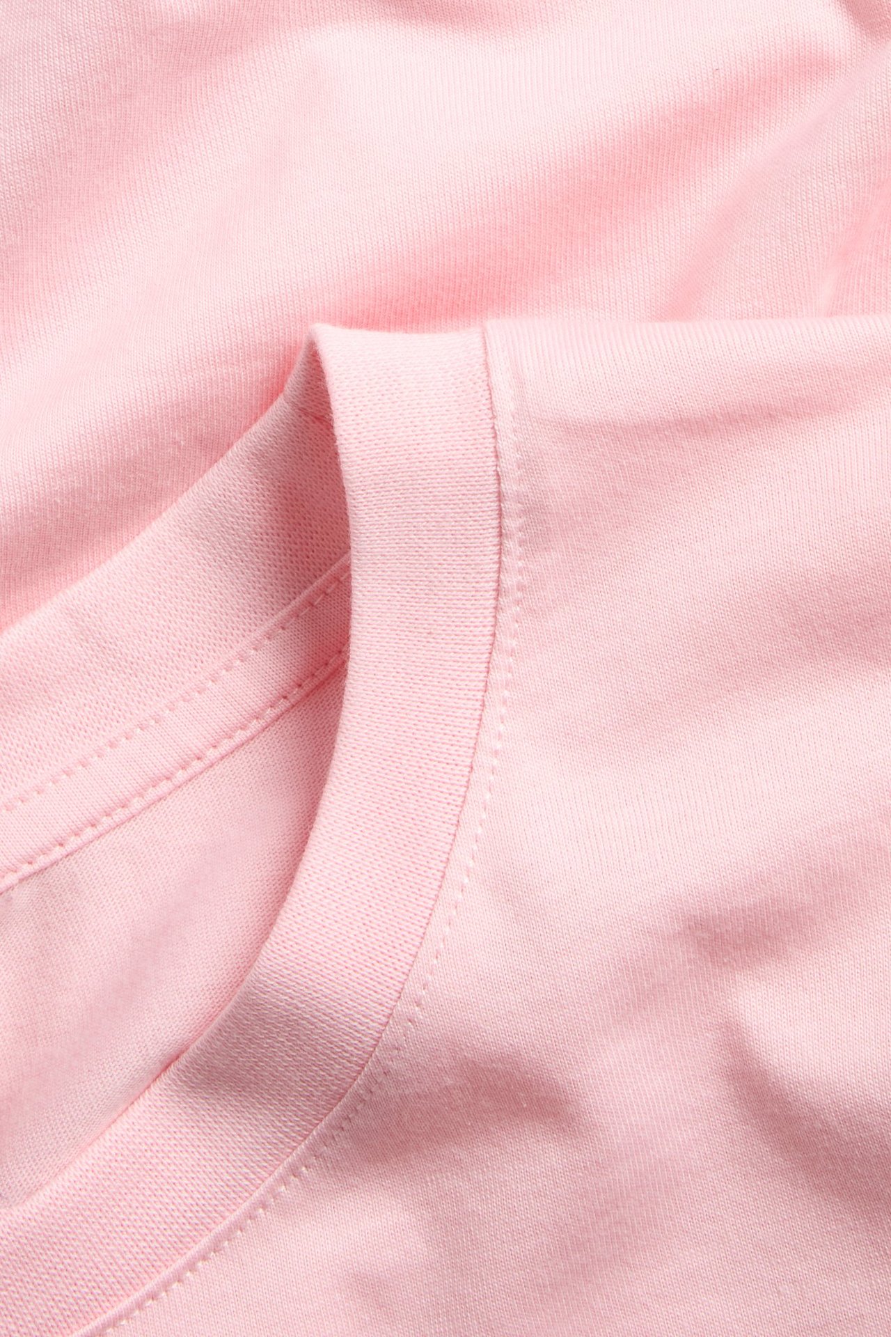 Nærbilde av en rosa, ensfarget, rett passform bomulls-T-skjorte, som viser den ribbestrikkede halslinningen og skuldersømmen.