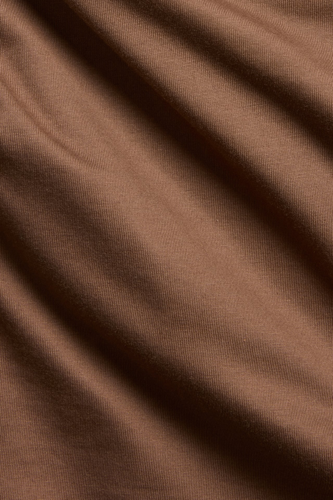Lähikuva ruskeasta, yksivärisestä puuvillakankaasta suoraleikkauksiseen T-paitaan, näyttäen tekstuurin.