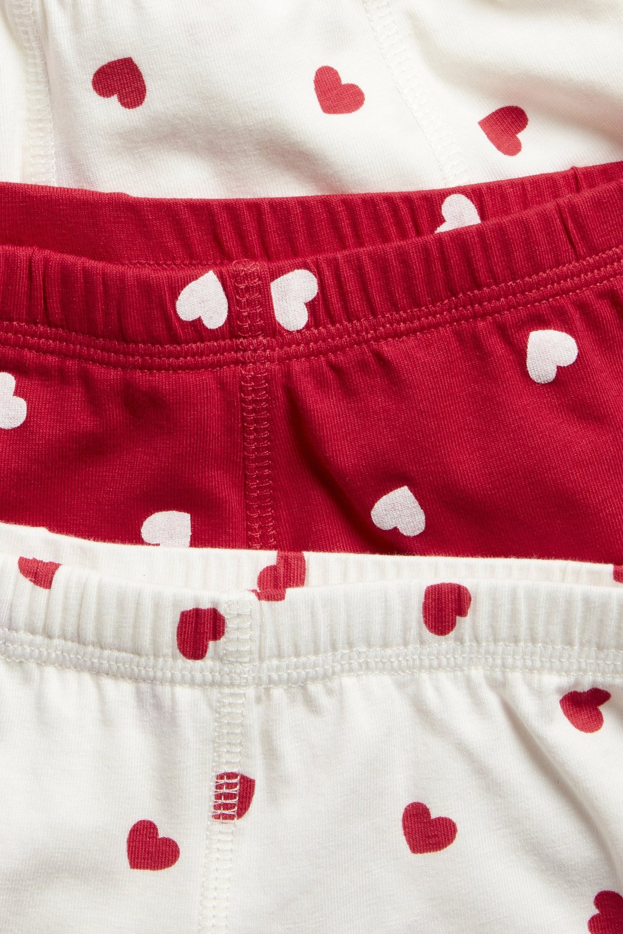 Lähikuva lasten luonnonvalkoisista ja punaisista sydänkuvioisista puuvillaboksereista, 3 kpl pakkaus, joustavat vyötäröt.