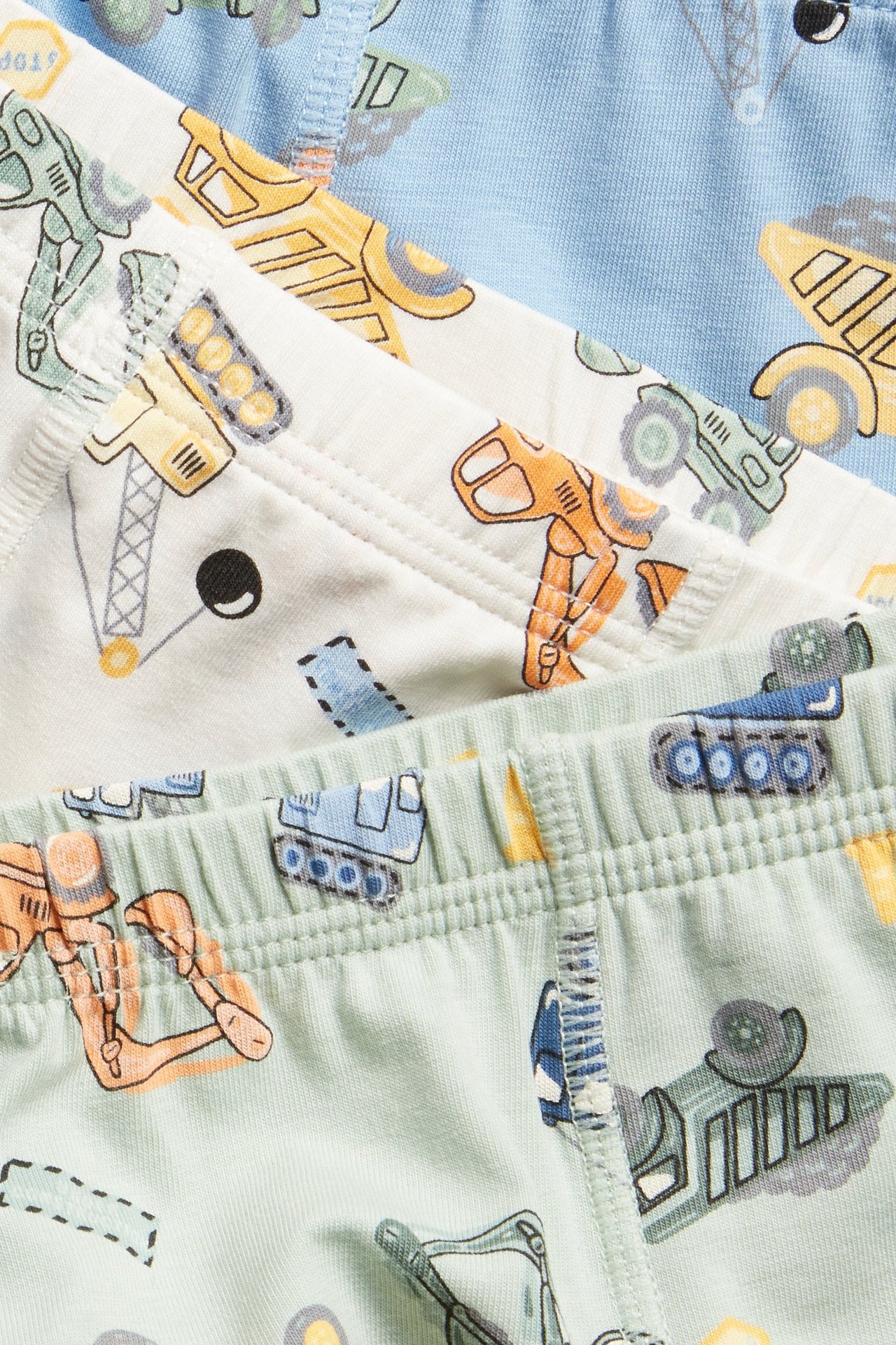 Lähikuva kolmesta lasten bokseripareista: vihreä, valkoinen, vaaleansininen rakennusajoneuvokuvioilla.