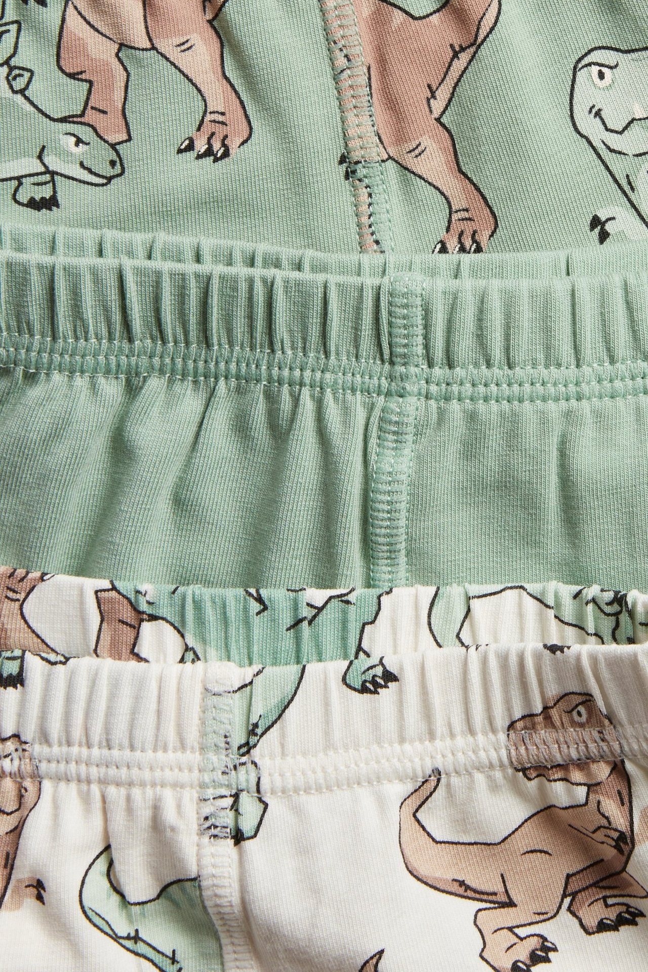 Zbliżenie na trzy dziecięce bokserki: jasnozielone w dinozaury, jednolicie jasnozielone i kremowe w dinozaury.