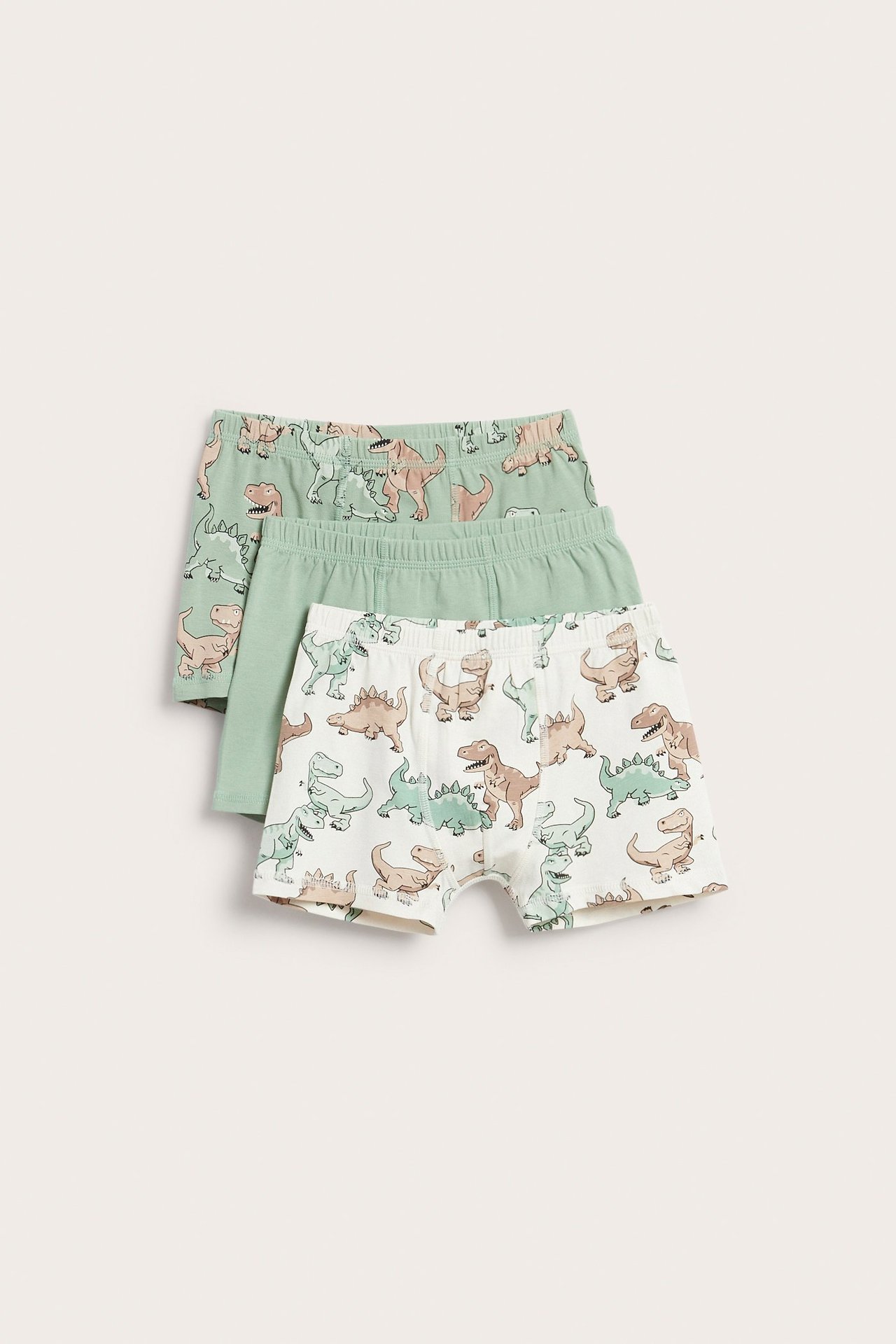 Widok z przodu 3-paku bokserek dziecięcych: jedne zielone, jedne zielone z dinozaurami i jedne ecru z dinozaurami.