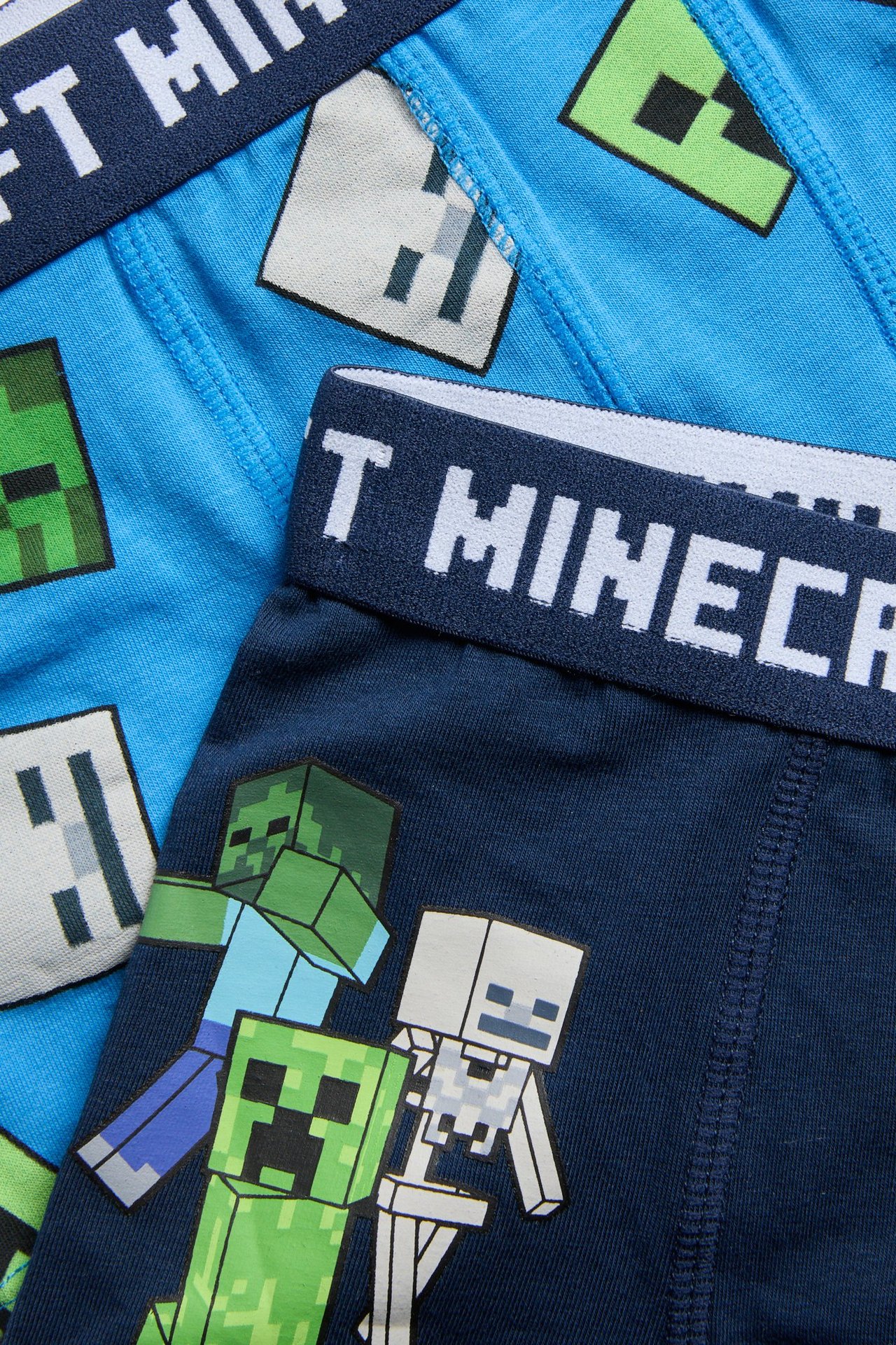Nærbilde: To par mørkeblå og lyseblå Minecraft boxershorts for barn med karaktertrykk.