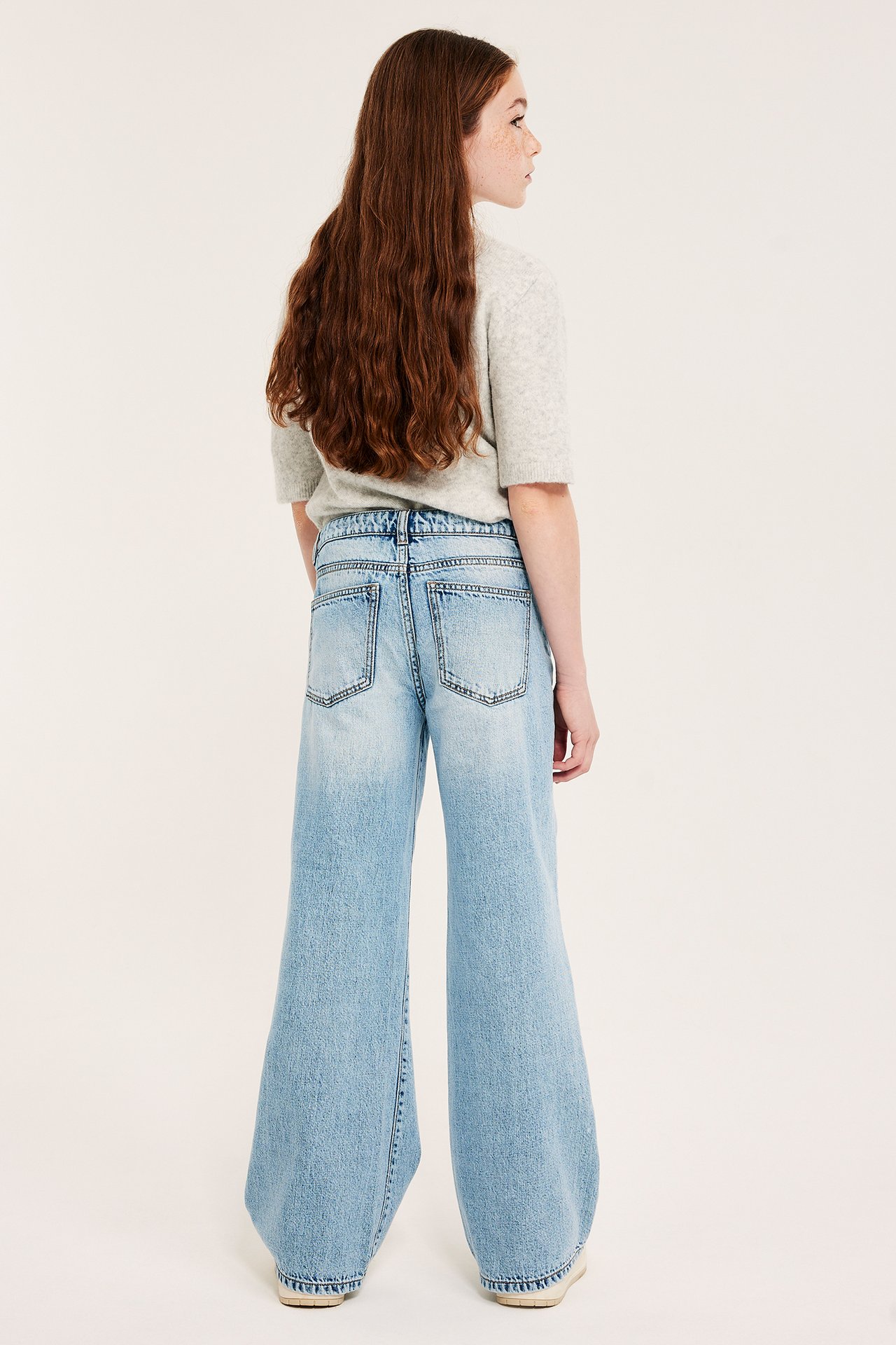 Bakfra, barn i lyseblå vide jeans med lavt liv og en lys grå kortermet topp.