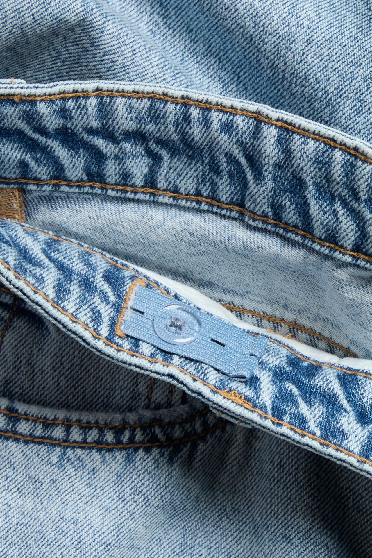 Zbliżenie na jasne dżinsy dziecięce z szerokimi nogawkami, pokazujące regulowany elastyczny pas i przezroczysty guzik.