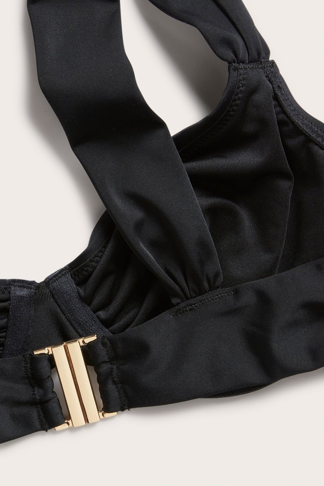 Närbild på svart draperad bygel-bikini-bh, breda axelband, framträdande guldfärgat ryggspänne.