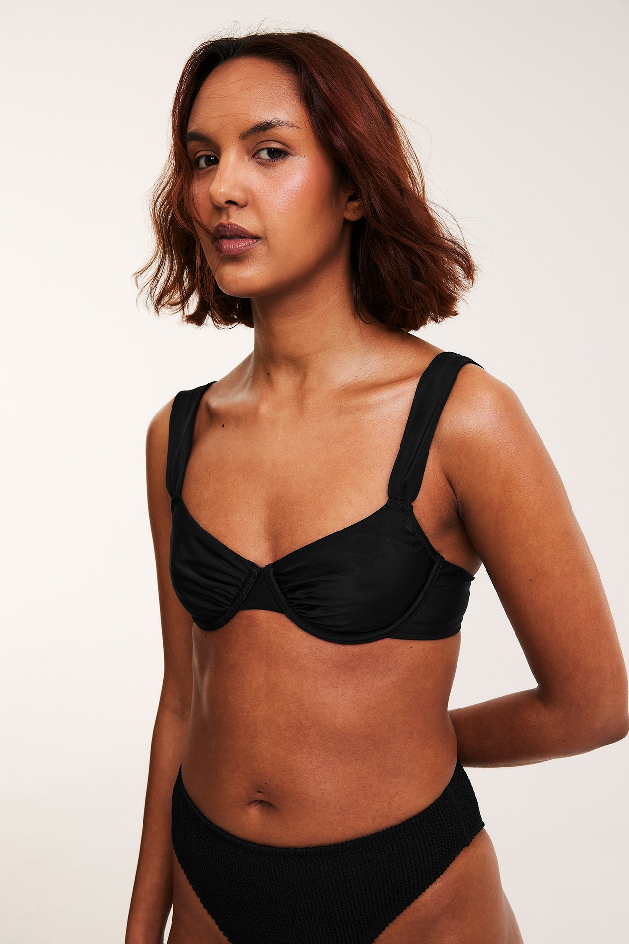 Edestäpäin, nainen mustassa kaarituellisessa bikiniliivissä leveillä olkaimilla ja kuvioiduilla alaosilla.