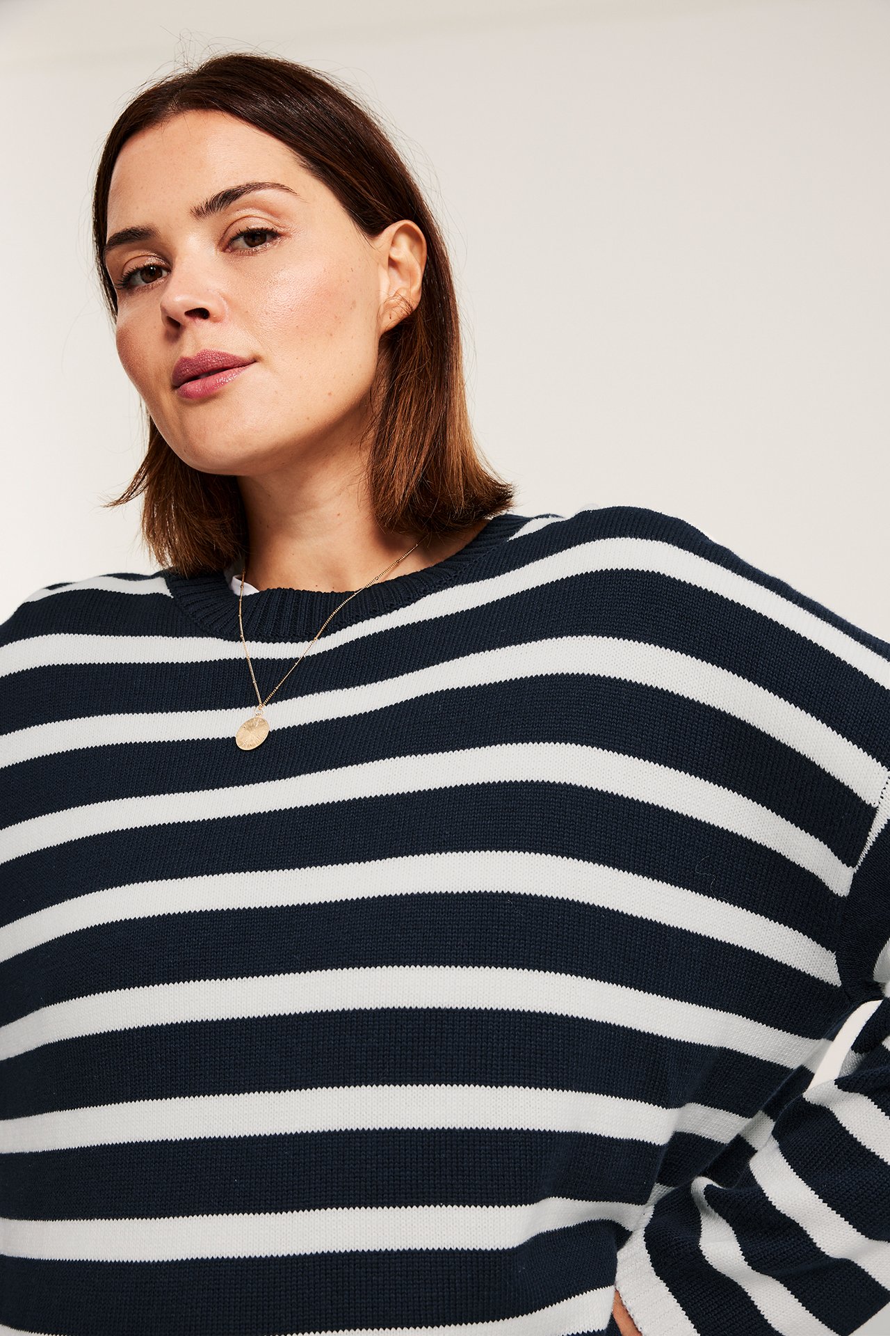 Edestä näkymä naisesta tummansinisessä ja valkoisessa raidallisessa neulepuserossa, yllään kultainen kaulakoru.