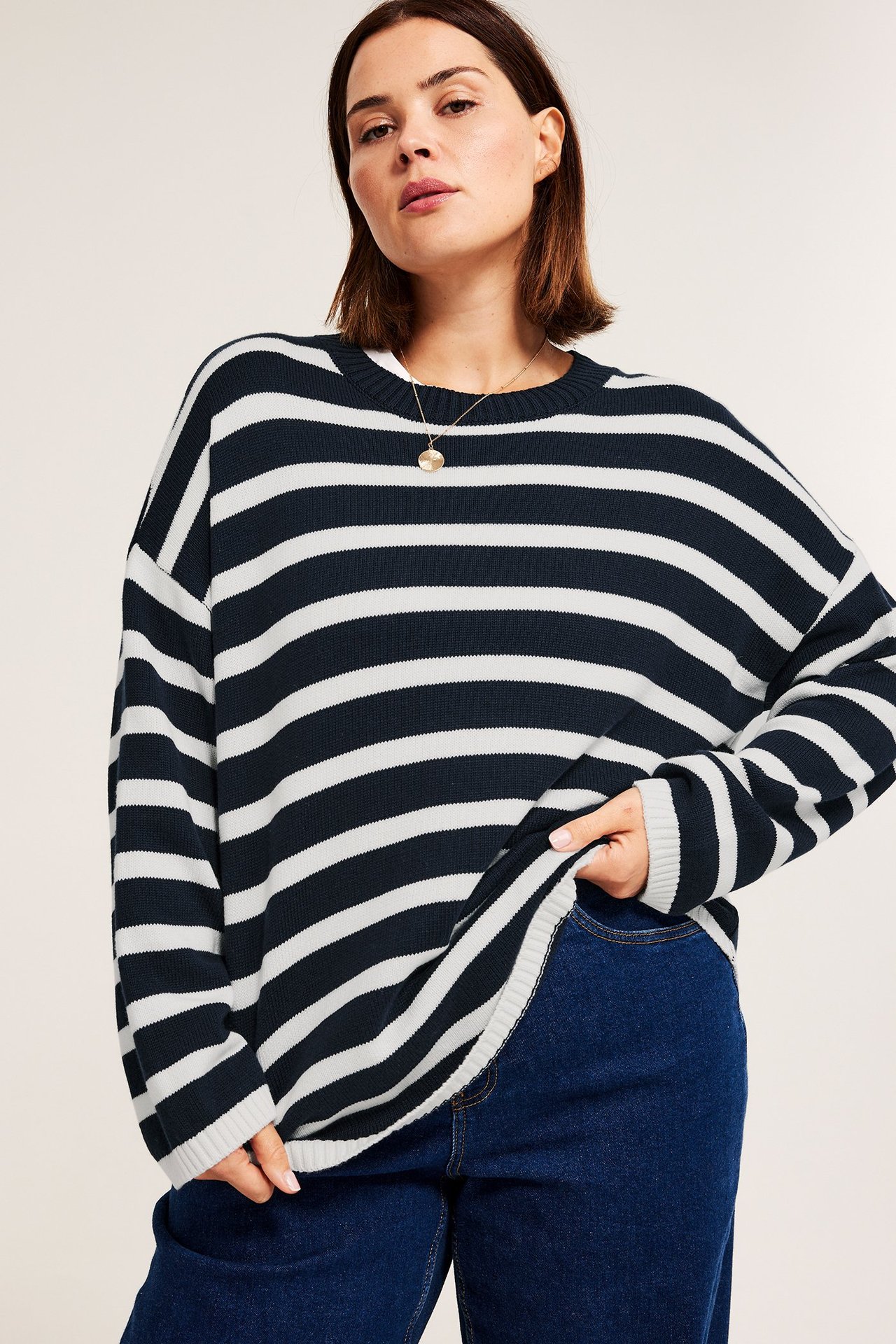 Edestäpäin: Nainen yllään rento laivastonsininen ja valkoraidallinen puuvillaneule, siniset farkut ja kultakaulakoru.