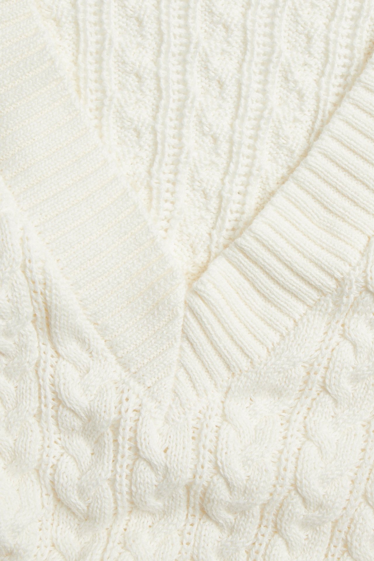 Nærbilde av en offwhite V-hals flettestrikket genser som viser det strukturerte mønsteret.