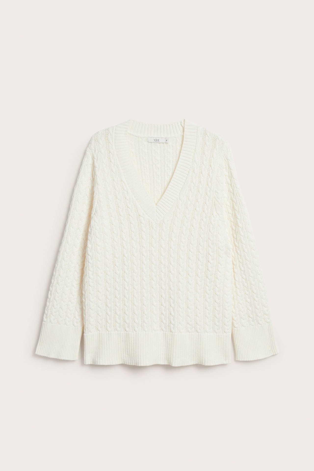 Frontvisning av en offwhite V-halset flettet genser i bomullsblanding.