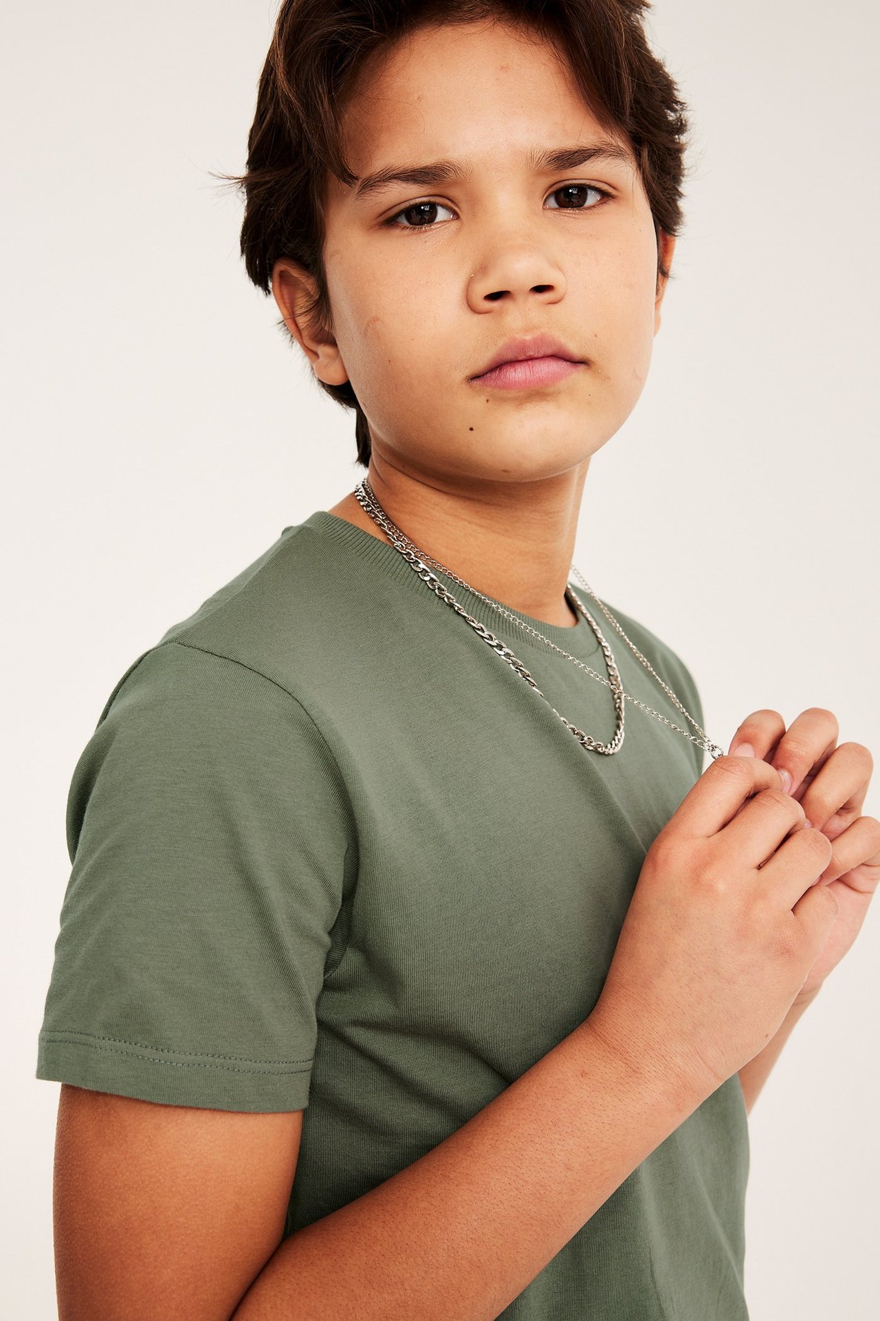 Lähikuva edestä lapsesta, jolla on vihreä puuvillainen T-paita ja hopeinen ketjukaulakoru käsissään.