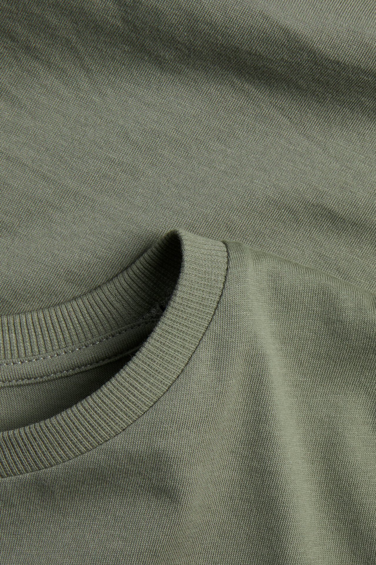 Lähikuva vihreästä yksivärisestä puuvilla-t-paidasta, jossa resori pyöreässä pääntiessä.