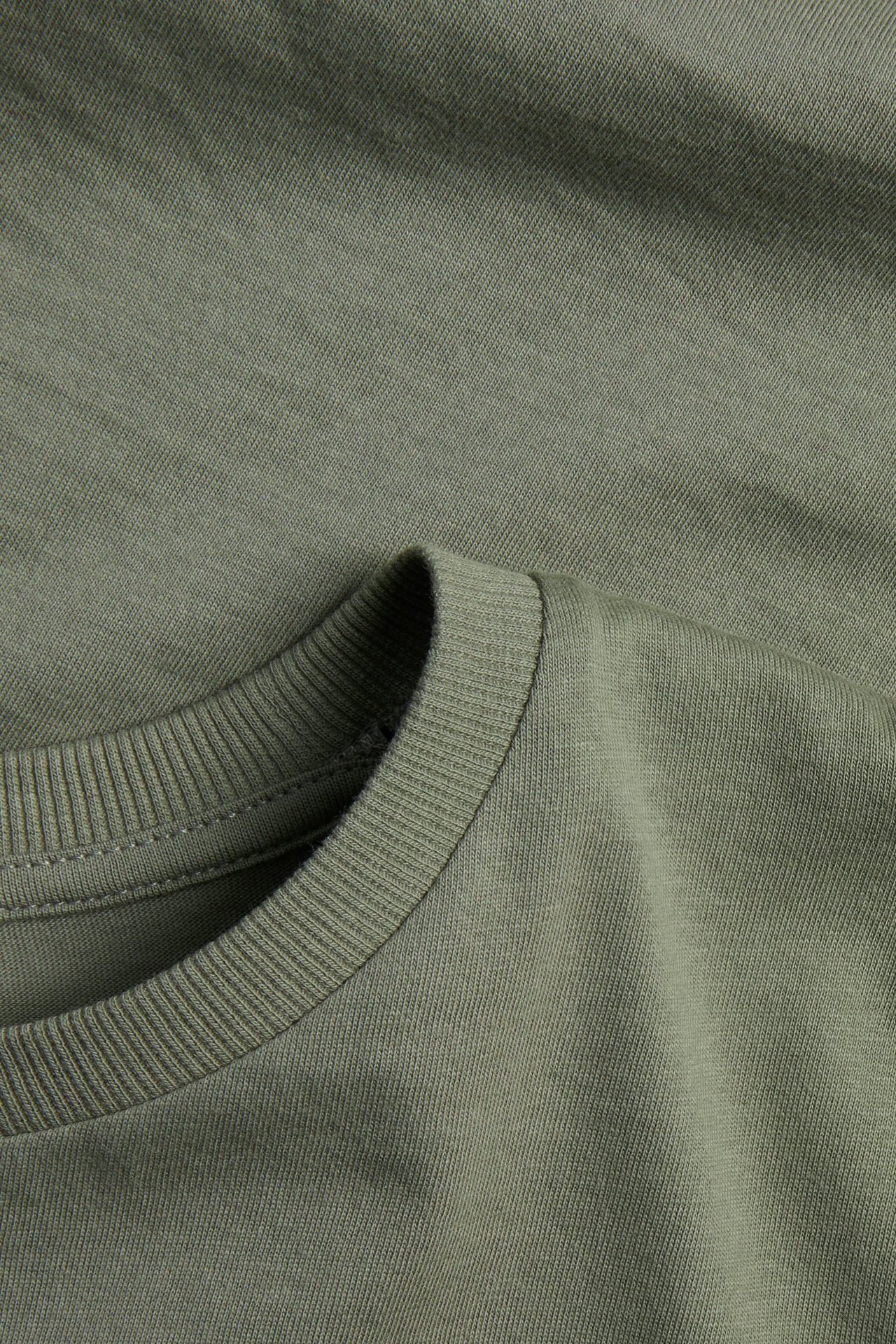 Zbliżenie zielonej bawełnianej koszulki o jednolitym kolorze z prążkowanym okrągłym dekoltem.