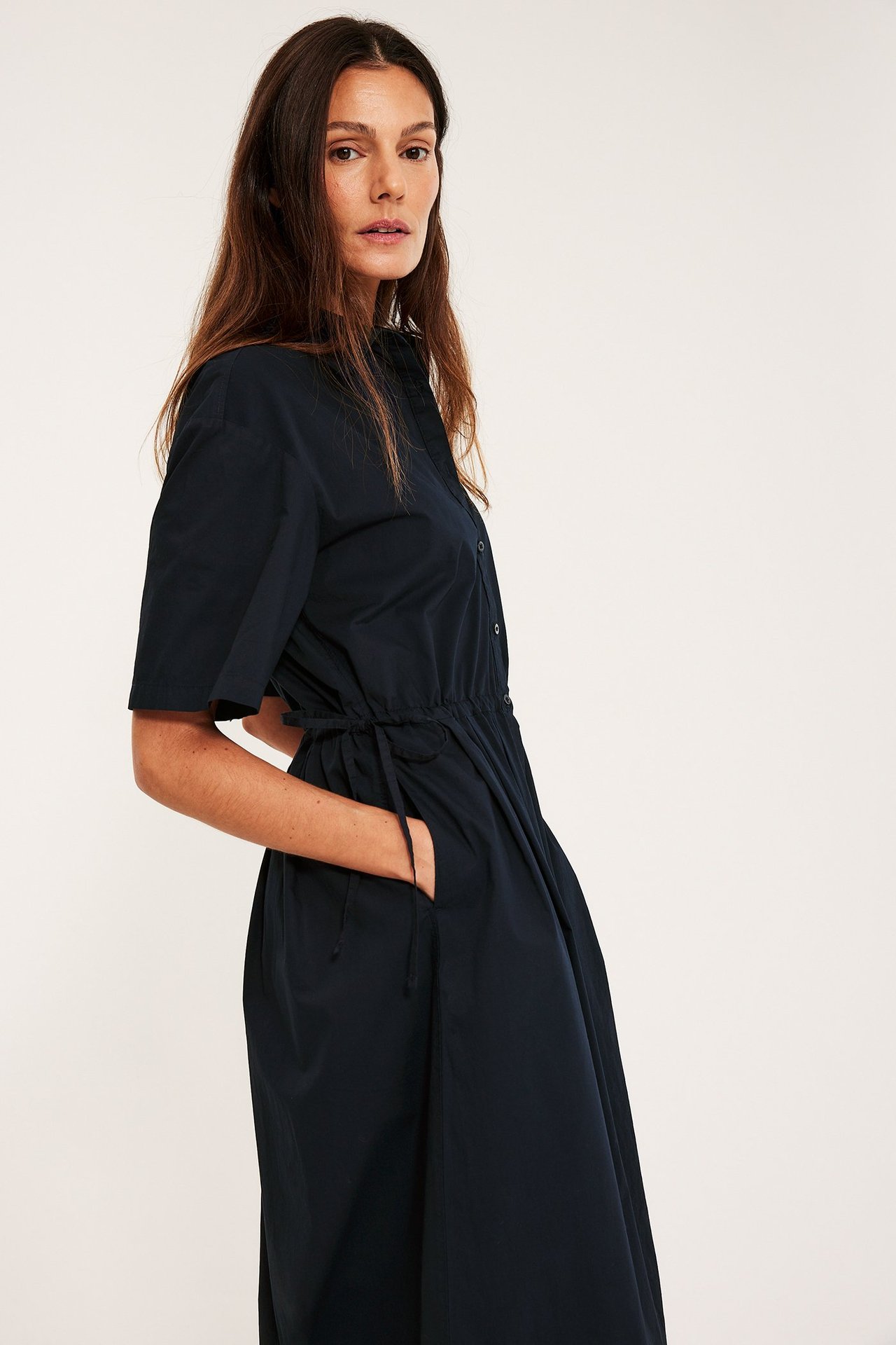 Sivusta: nainen tummansinisessä puuvillapaitamekossa, lyhyet hihat, nyörivyötärö, sivutaskut.