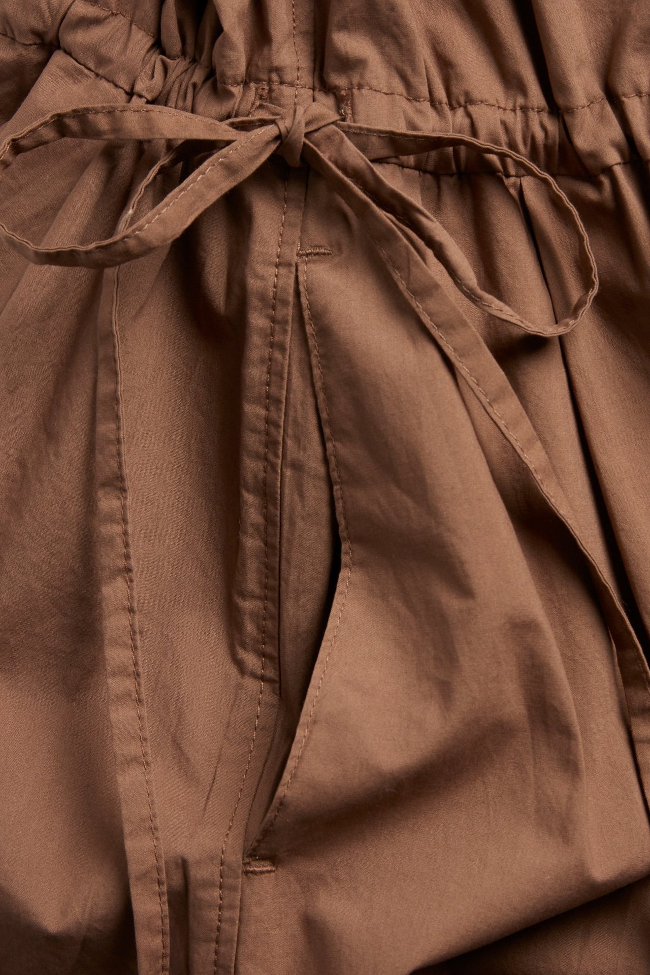 Zbliżenie na brązową bawełnianą sukienkę koszulową z wiązanym ściągaczem w pasie i boczną kieszenią.