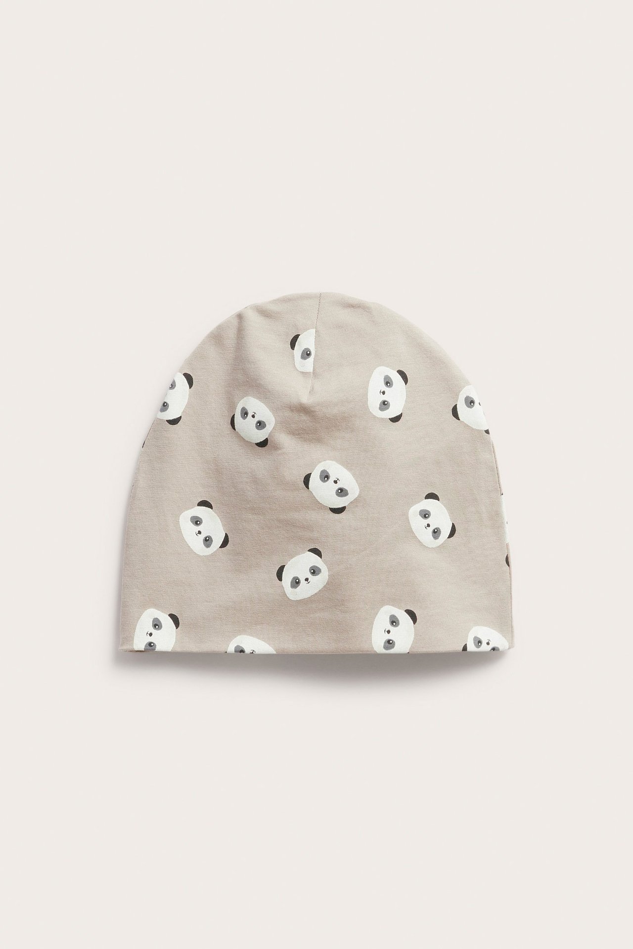 Framifrån: en beige baby mössa i single jersey med upprepade svarta och vita panda tryck.