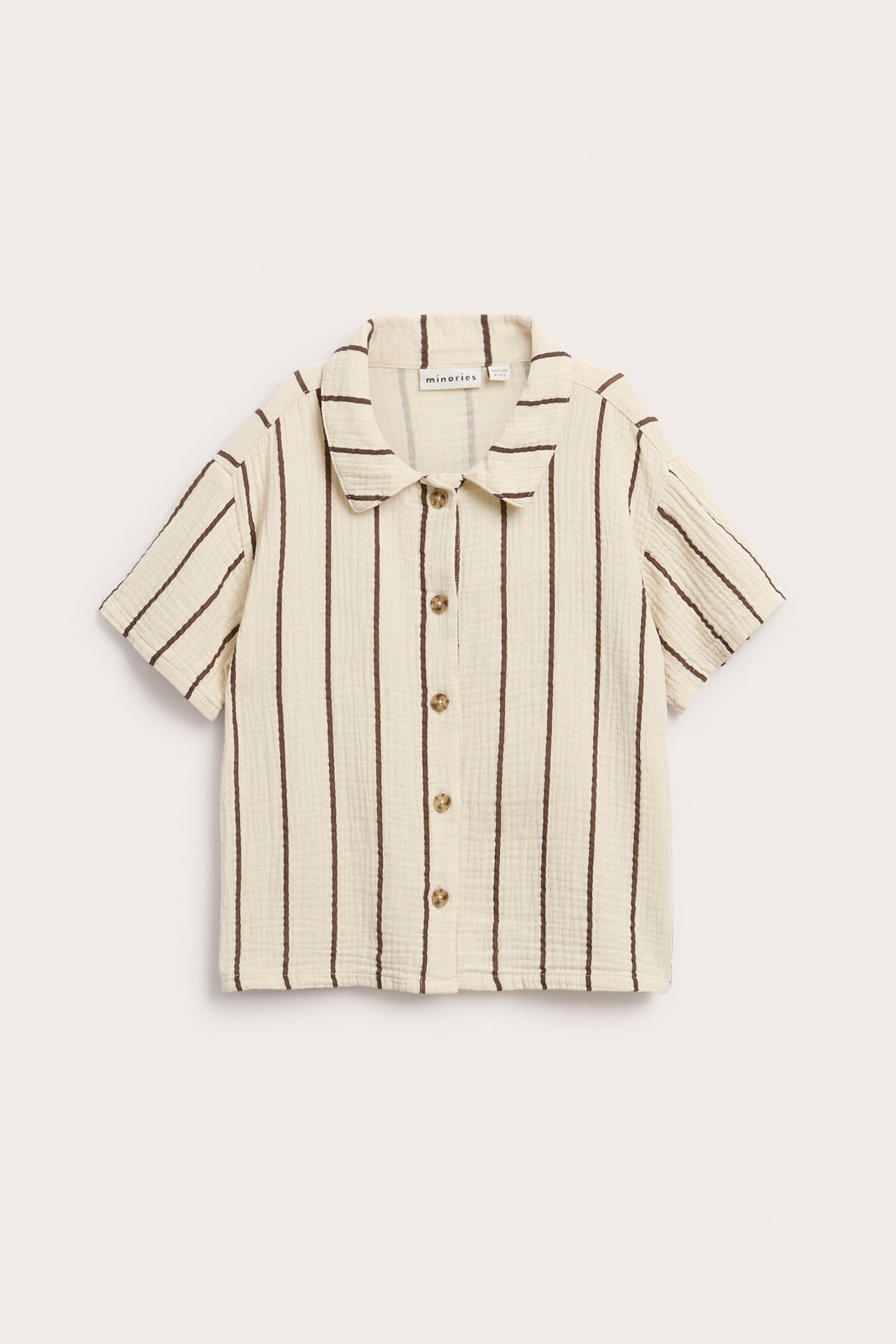 Framifrån: Barns krämfärgad kortärmad musslinskjorta med bruna vertikala ränder och knappar fram.