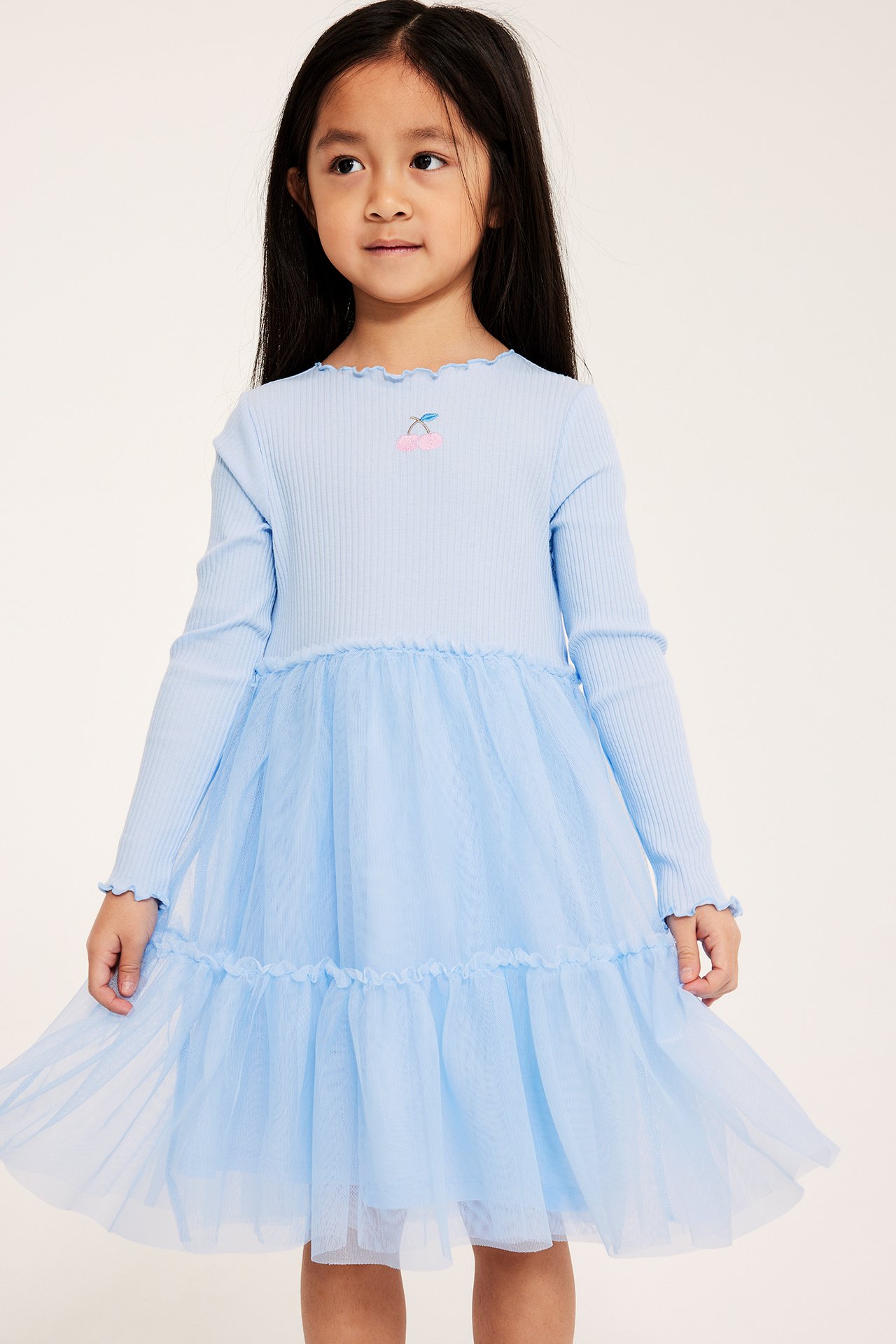 Framsida av ett barn i ljusblå klänning med ribbad topp, broderat körsbär och en volangkjol i mesh.