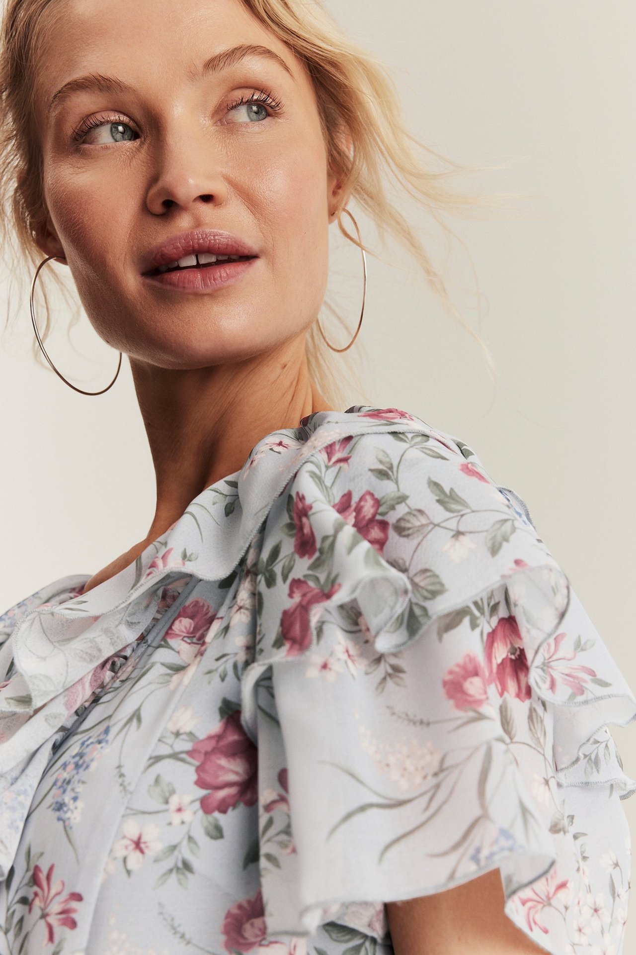 Närbild på kvinna i ljusblå blommig chiffongklänning med volanger och guldfärgade örhängen.