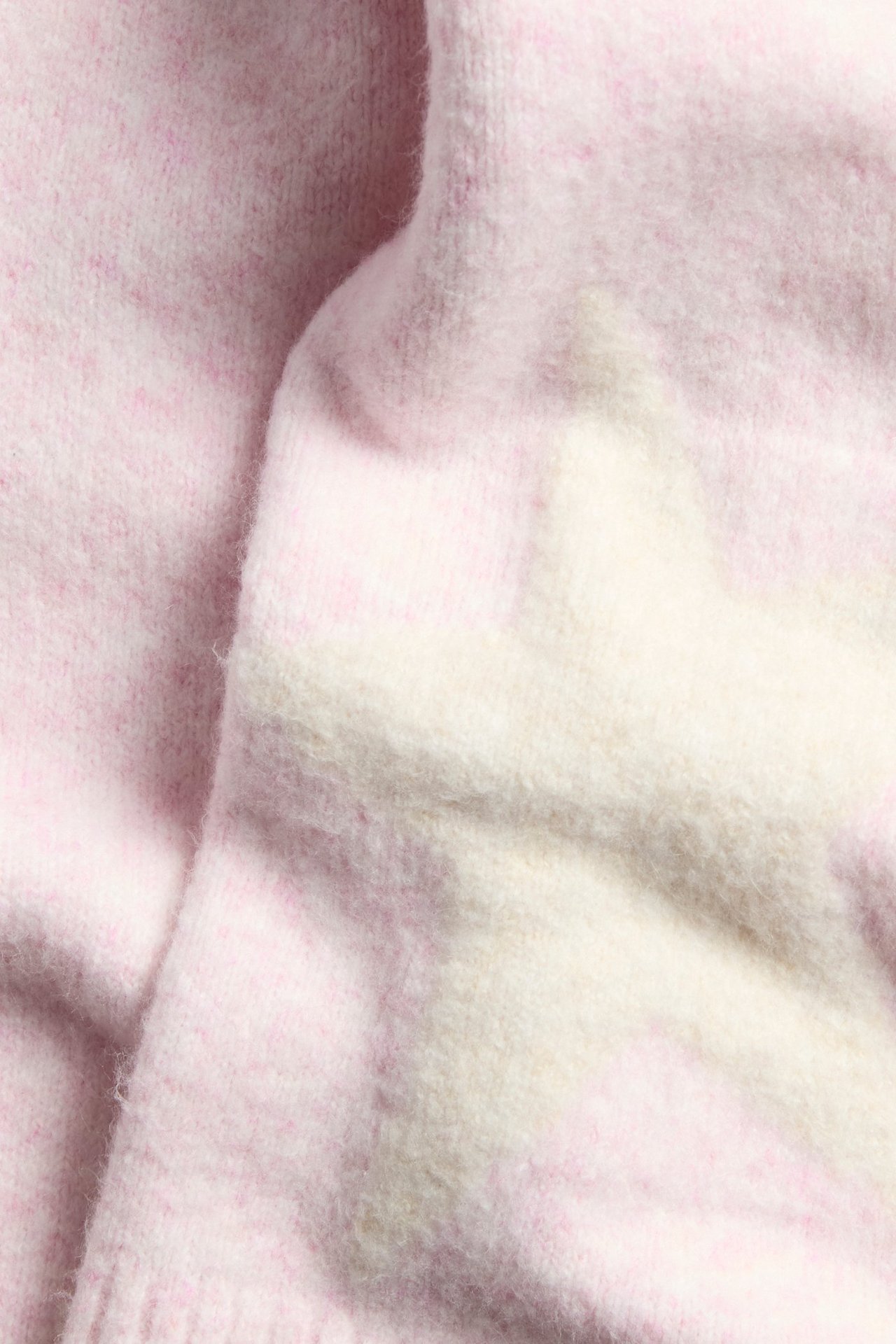 Nærbilde av en rosa strikkegenser med et off-white jacquardmønster med stjerner.