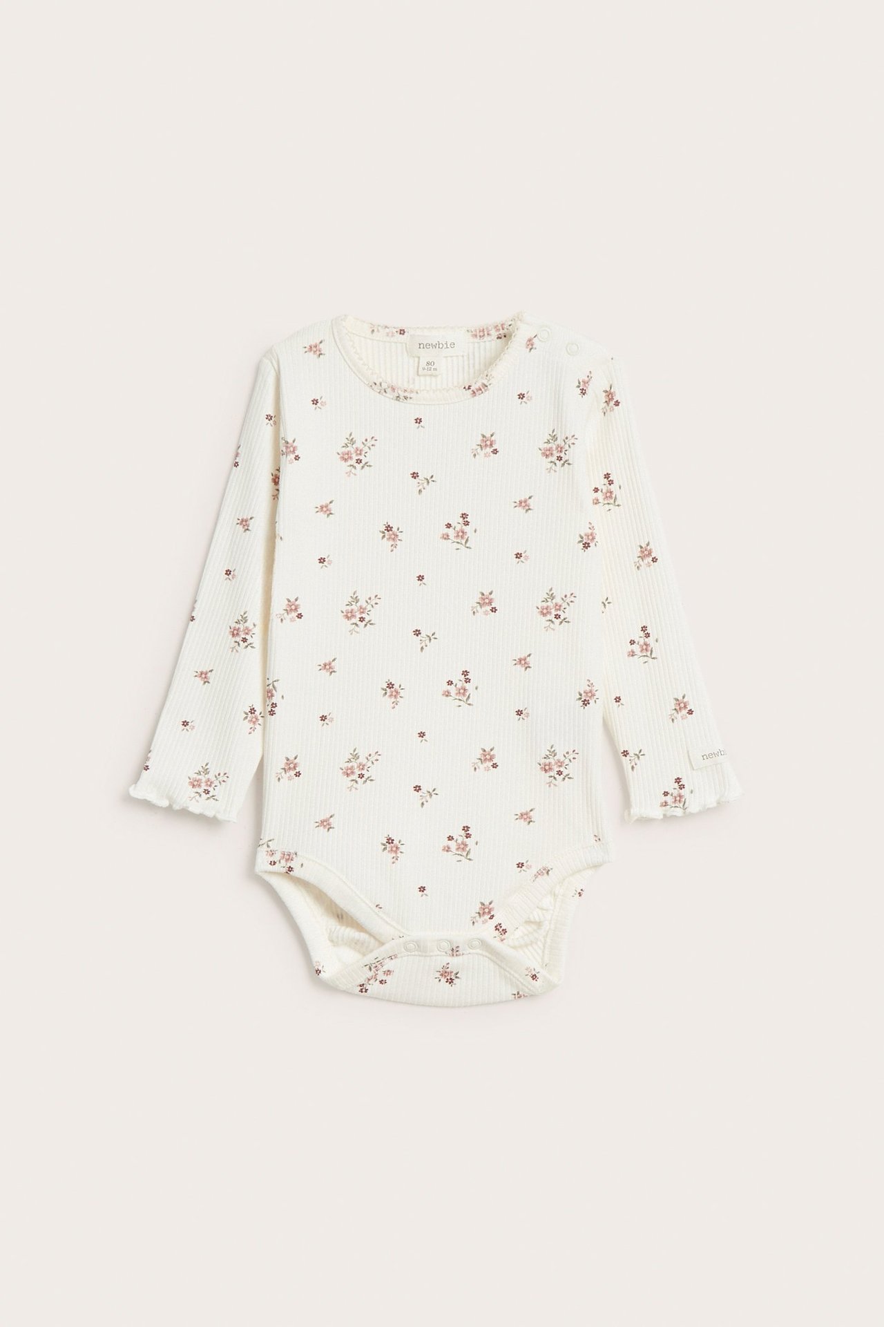 Edestäpäin, luonnonvalkoinen vauvan ribbipaita vaaleanpunaisella kukkakuviolla, pitkät hihat aaltoilevilla reunoilla ja nepparit.