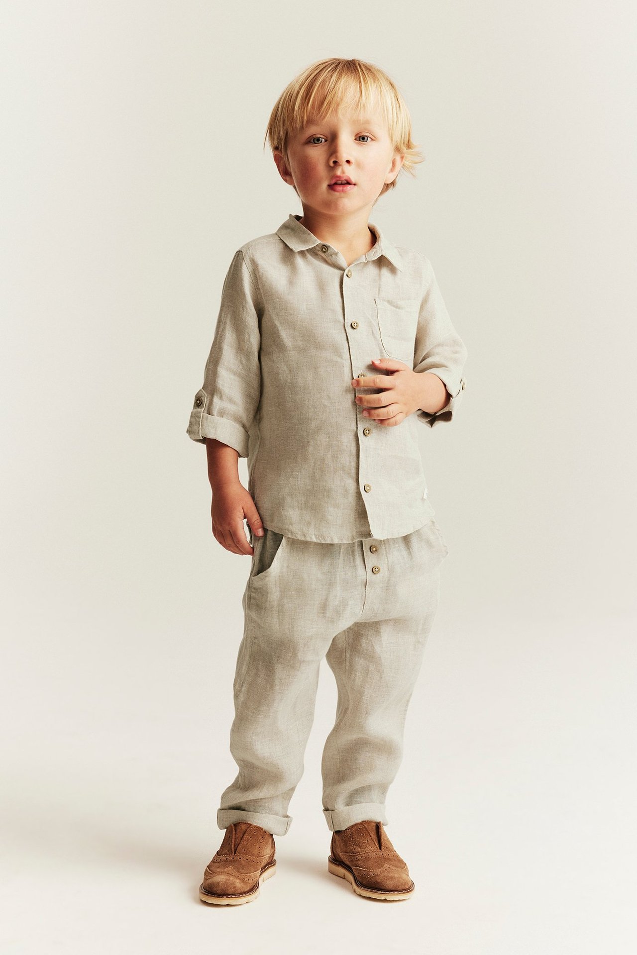 Widok z przodu: dziecko w jasnobeżowych lnianych spodniach z podwiniętymi nogawkami i pasującej koszuli.