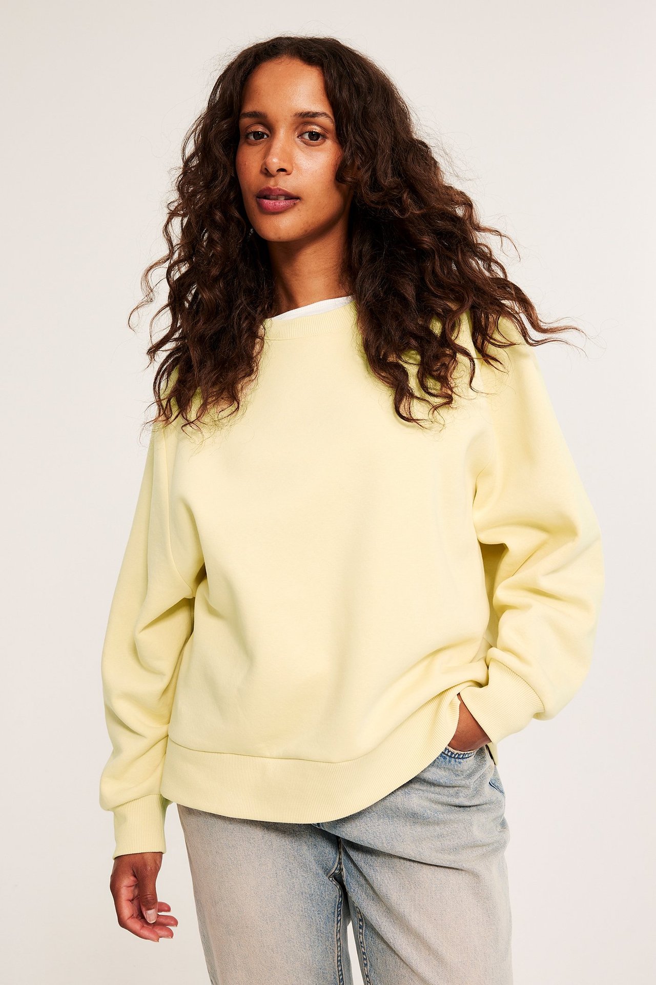 Naisen etukuva, yllään vaaleankeltainen collegepaita, valkoinen t-paita ja vaaleansiniset farkut.