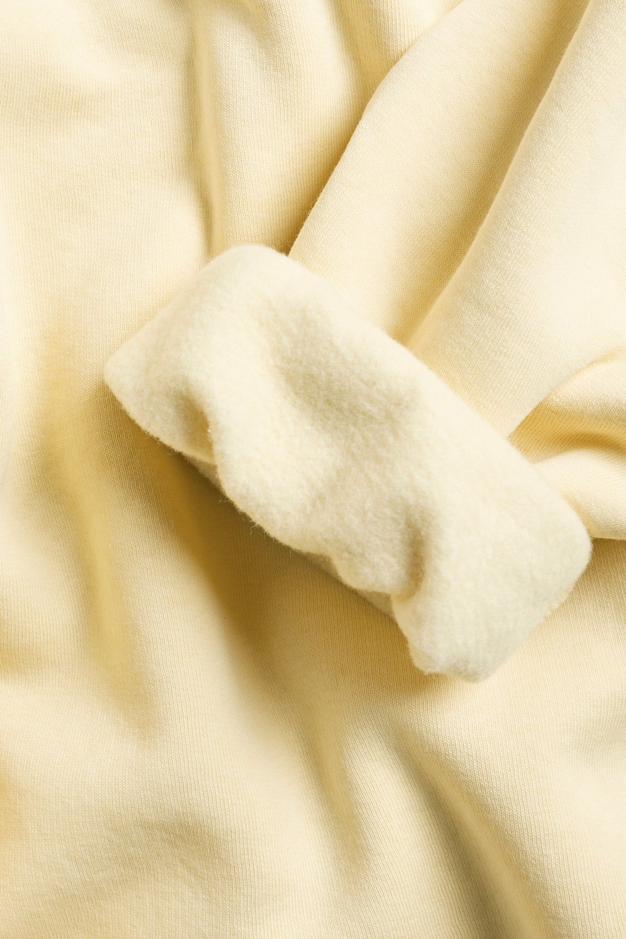 Zbliżenie na jednolitą żółtą bluzę dresową, ukazujące miękki materiał i złożony mankiet.