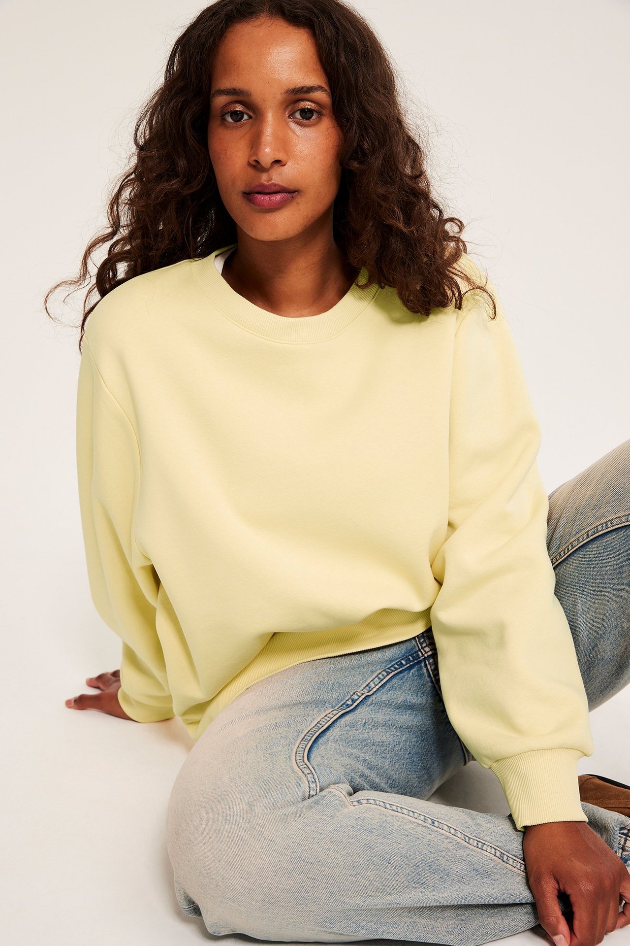 Widok z przodu kobiety w żółtej bluzie z okrągłym dekoltem i jasnoniebieskich dżinsach.
