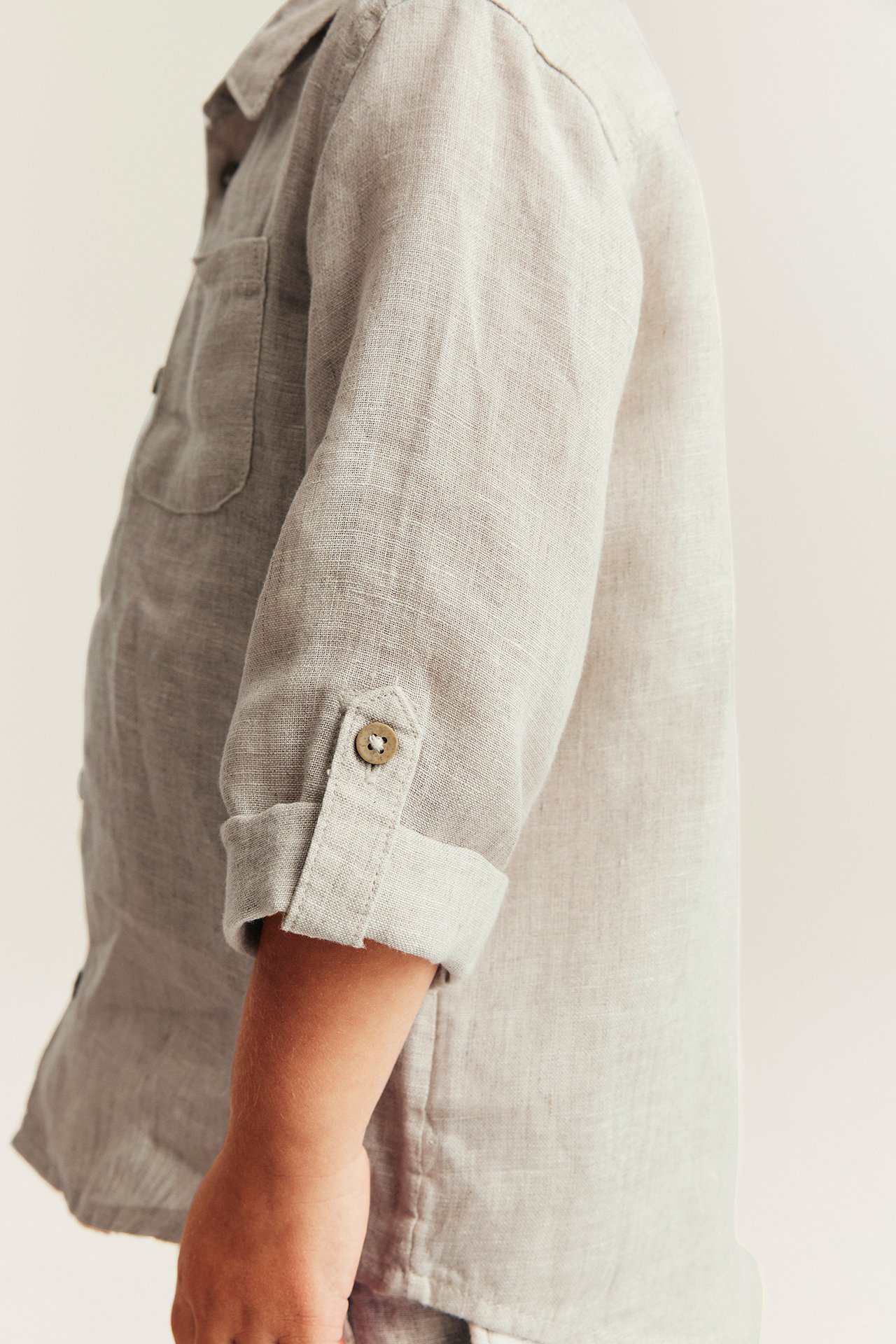 Lähikuva lapsesta vaaleanbeigessä pellavapaidassa, jossa on käärityt hihat ja rintatasku.