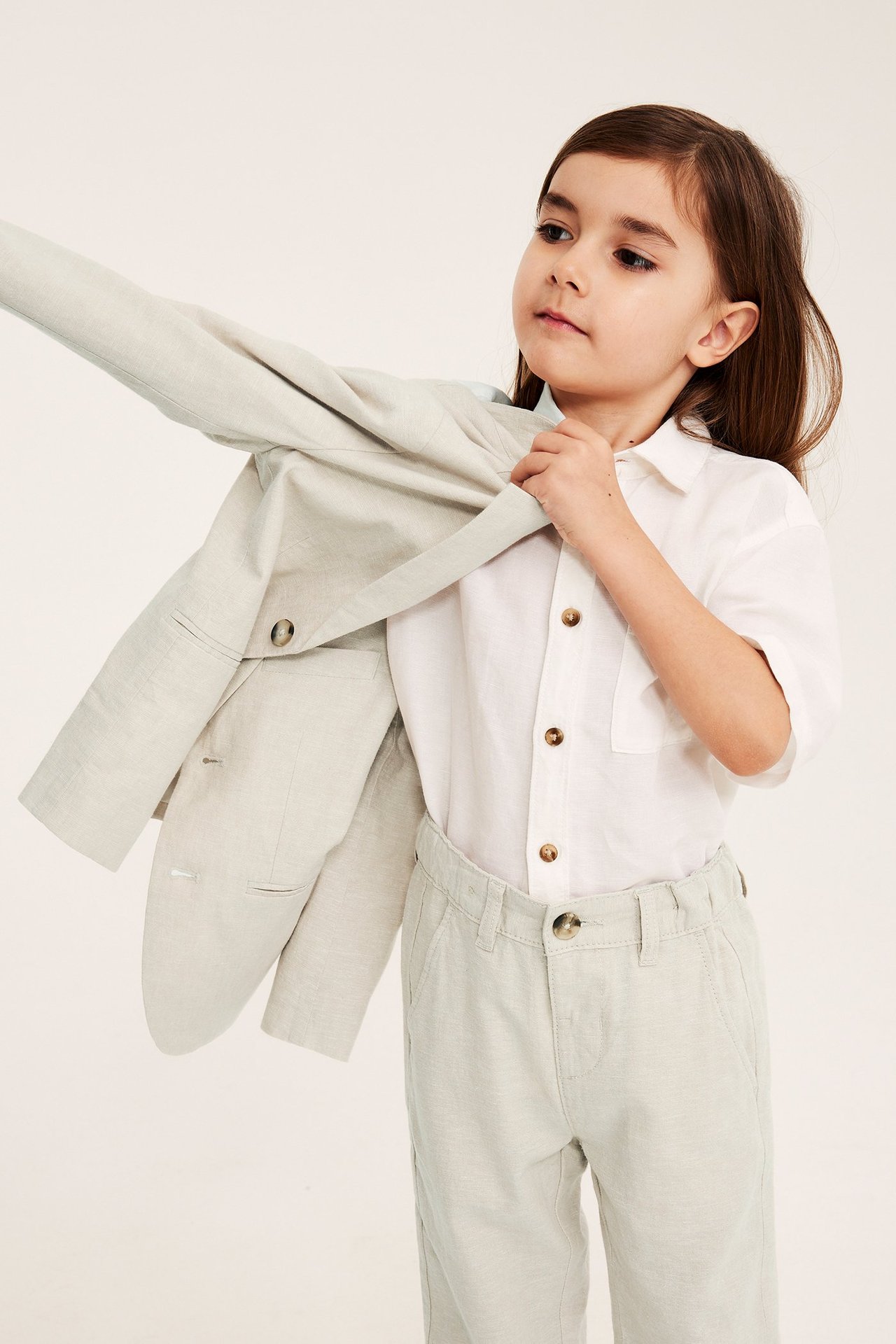 Frontutsikt: Barn tar på lys beige linblazer over en hvit skjorte og lys beige bukse.