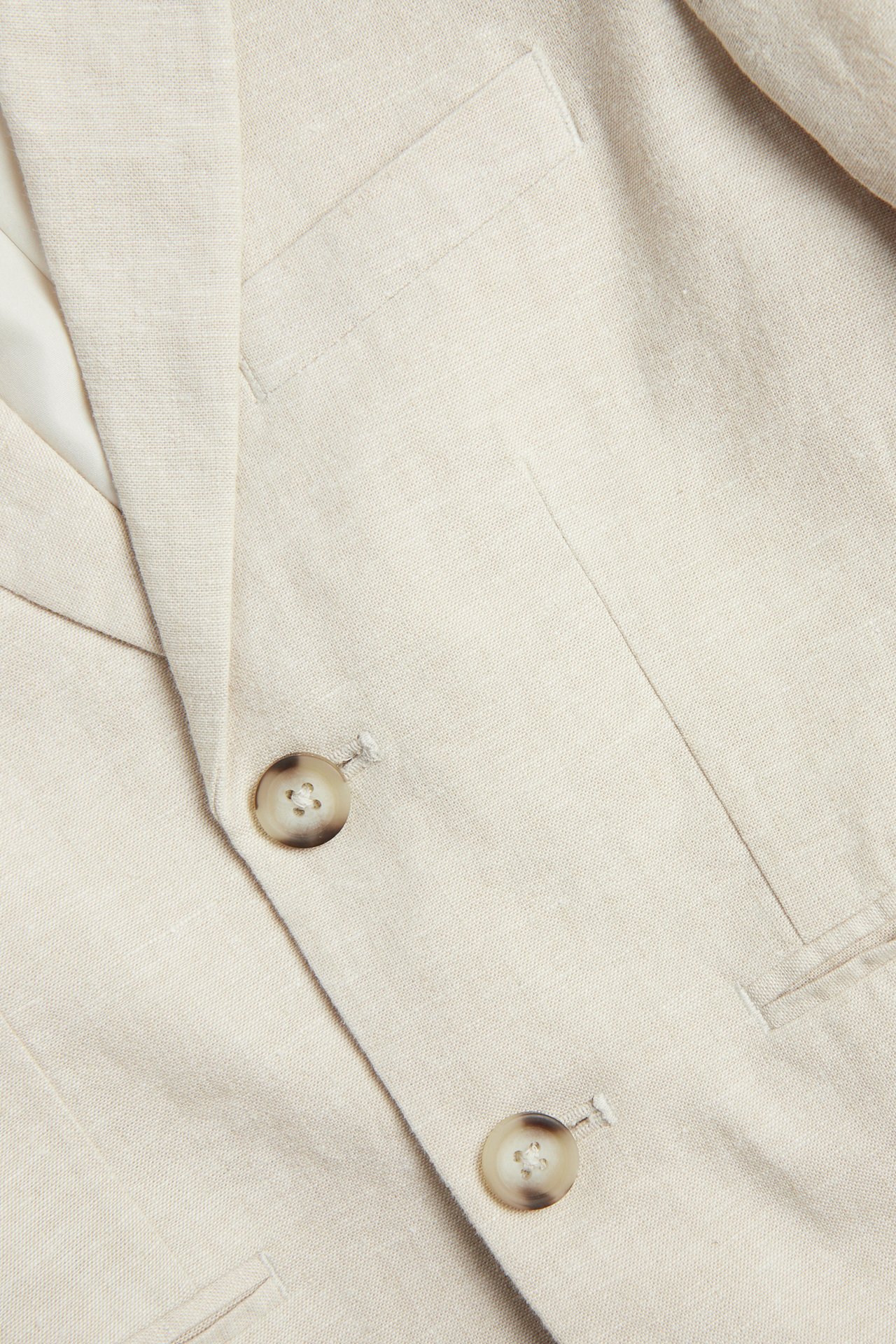 Nærbilde av en lys beige linblanding blazer med to knapper og lommer.