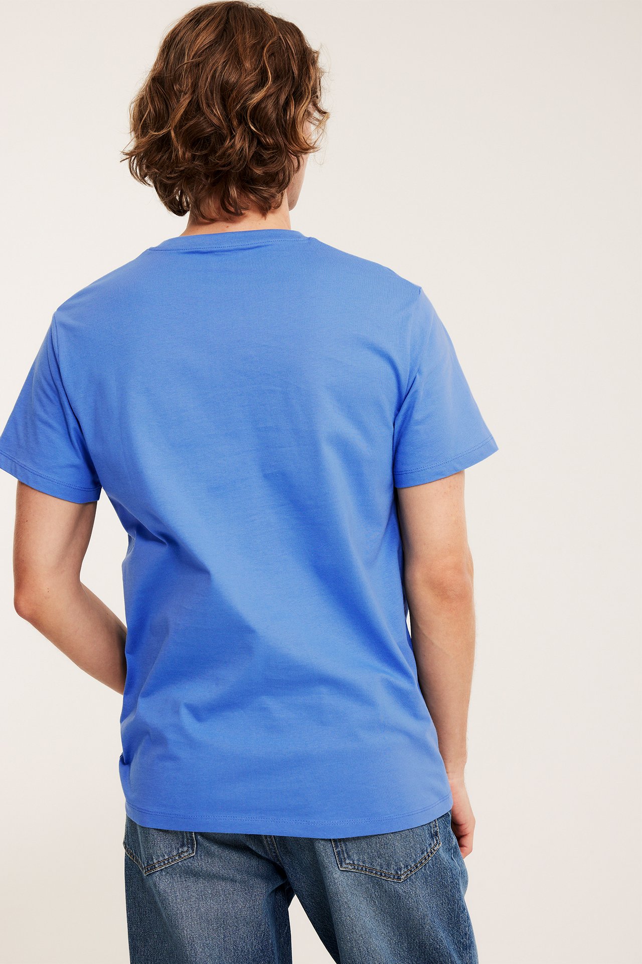 Mann bakfra i en lyseblå, rundhalset t-skjorte og blå jeans.