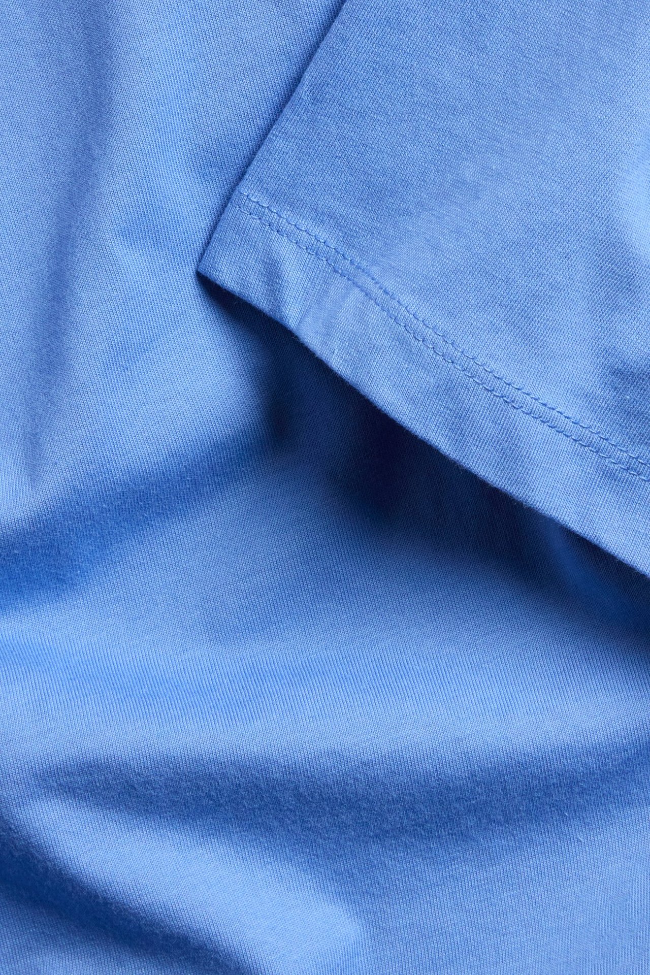 Zbliżenie jasnoniebieskiego męskiego T-shirtu z bawełny organicznej, widoczna faktura i szew.