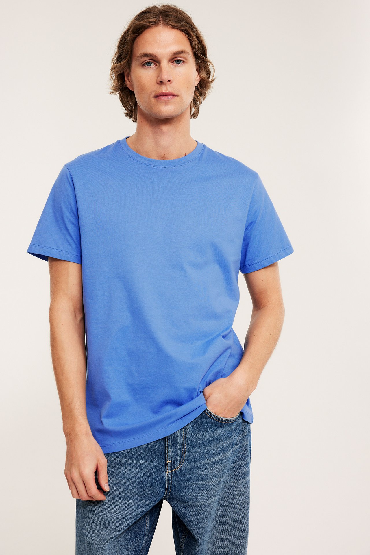 Edestä päin, mies yllään vaaleansininen puuvillainen pyöreäkauluksinen t-paita ja siniset farkut.